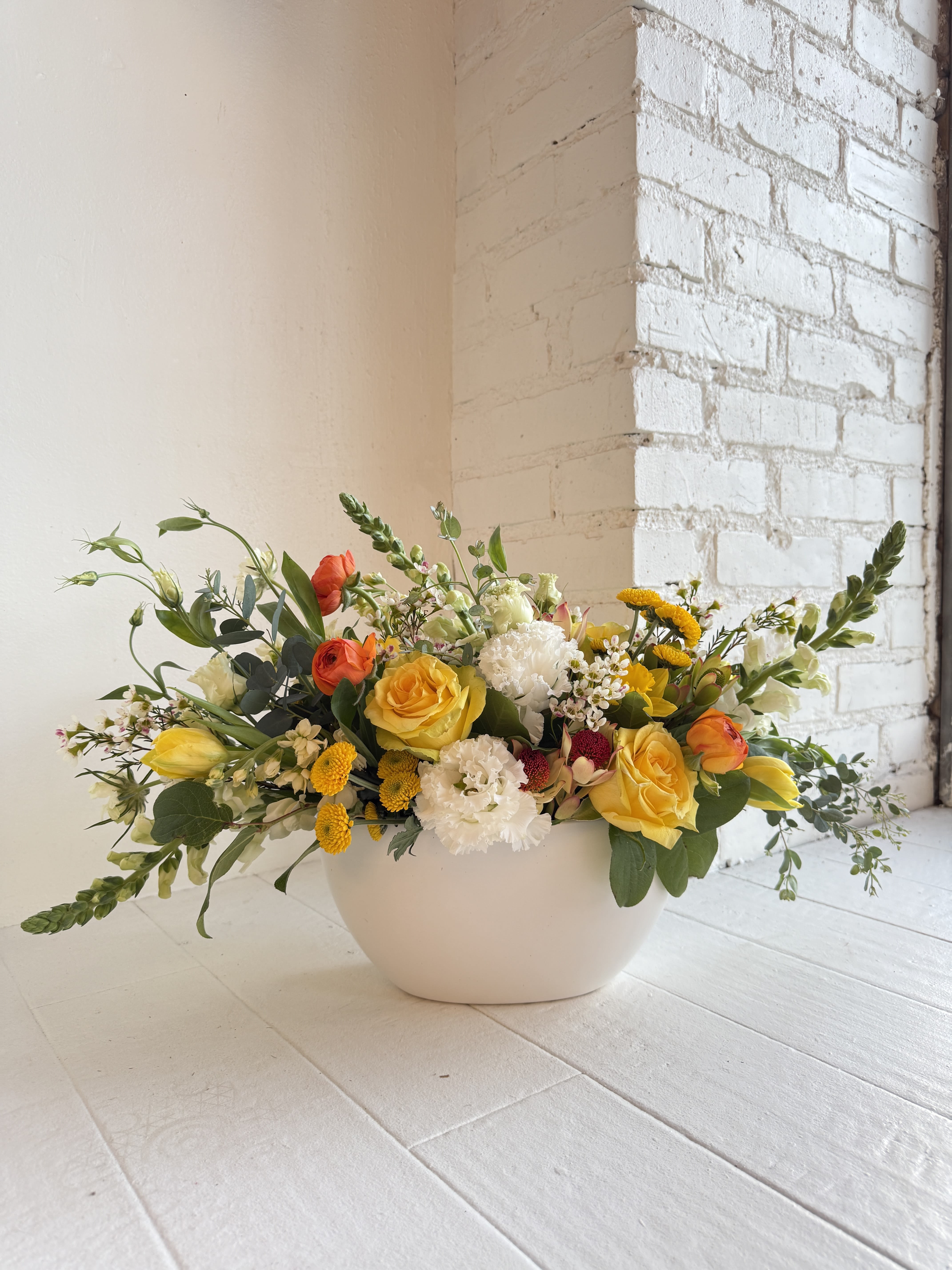 Clementine - Clementine is stunning. We start with a white ceramic long low container and carefully select all our favorite flowers in shades of buttery soft yellows, orange, green and white. This arrangement is abundant, lush, stylish and creative. We favor using all the best seasonal flowers. Ranunculus, roses, snapdragons, anemones, peonies, hydrangea, stock, lisianthus.