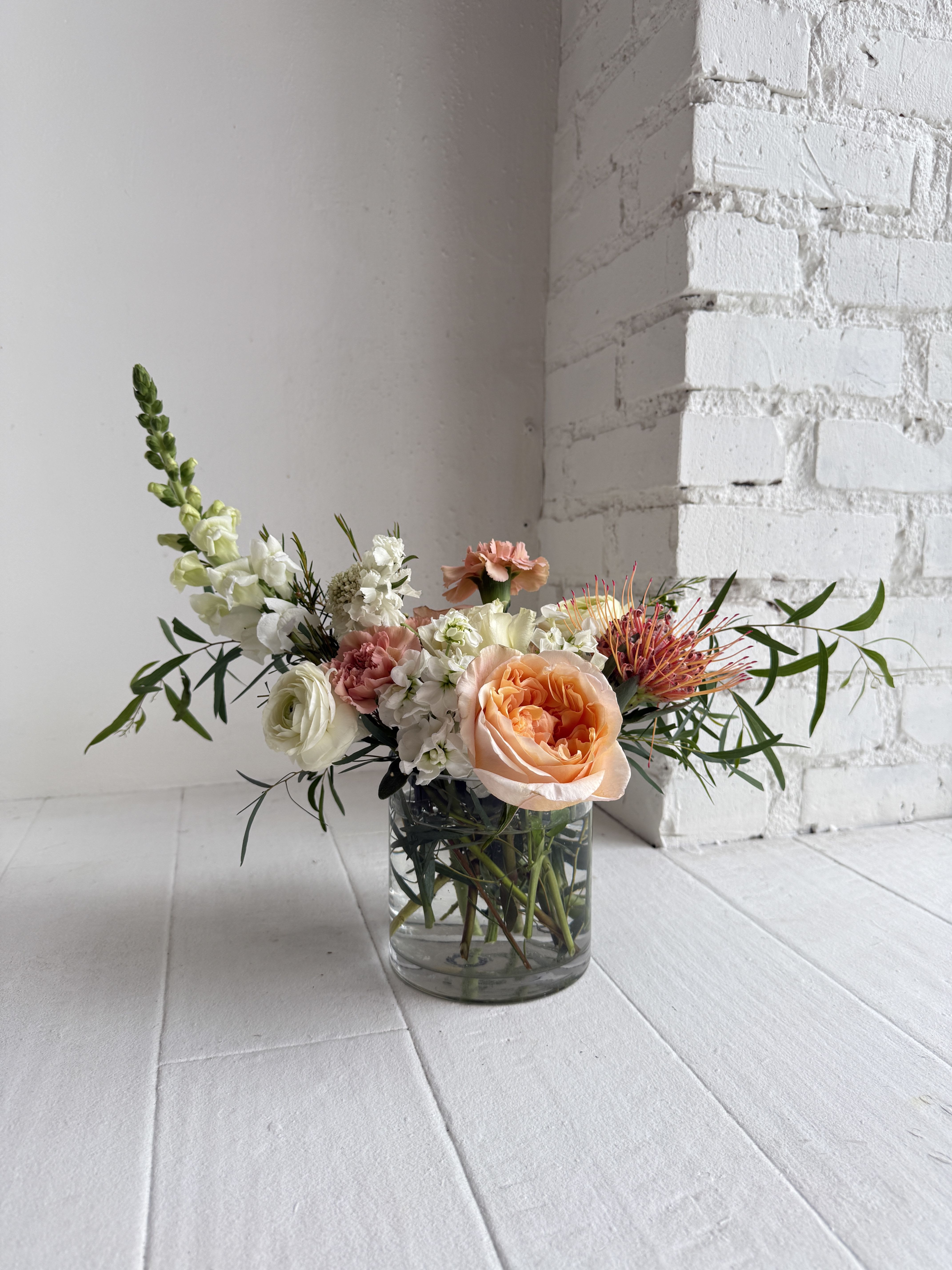 Emma - Emma. We gather our favorite blooms in shades of peach, creamy whites and greens. We use a clear glass vase, with all focus on the flowers contained within. Our favorite flowers for this arrangement are garden roses, heirloom mums, lisianthus, ranunculus, wax flower, stock, poppies, tulips and other rare varieties and finished with greens. Emma is available in 3 sizes. View options at check out.
