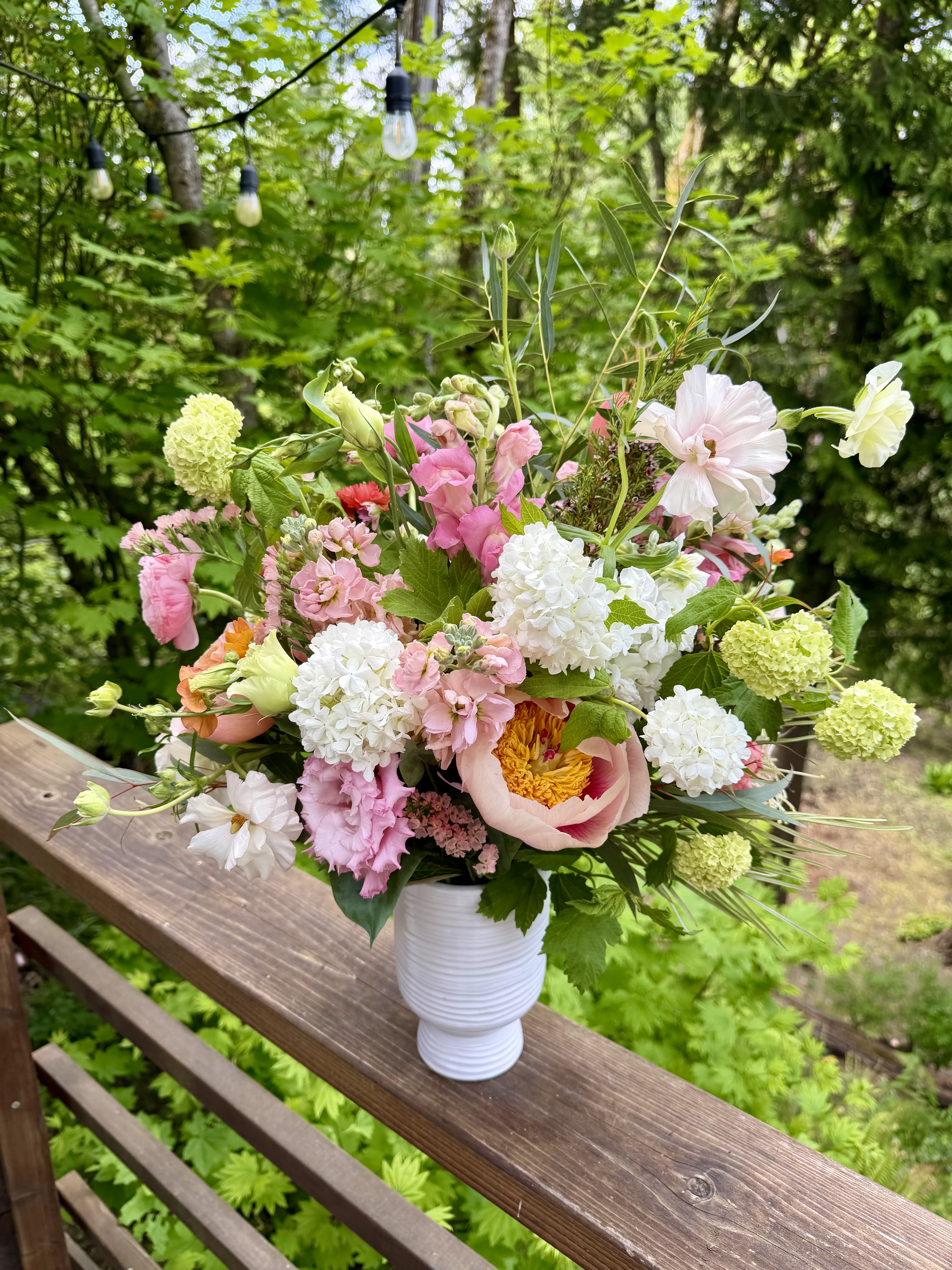 Naomi - Garden style arrangement in a taller white ceramic vase. Different shades of pinks, some peach, white, and greens.  