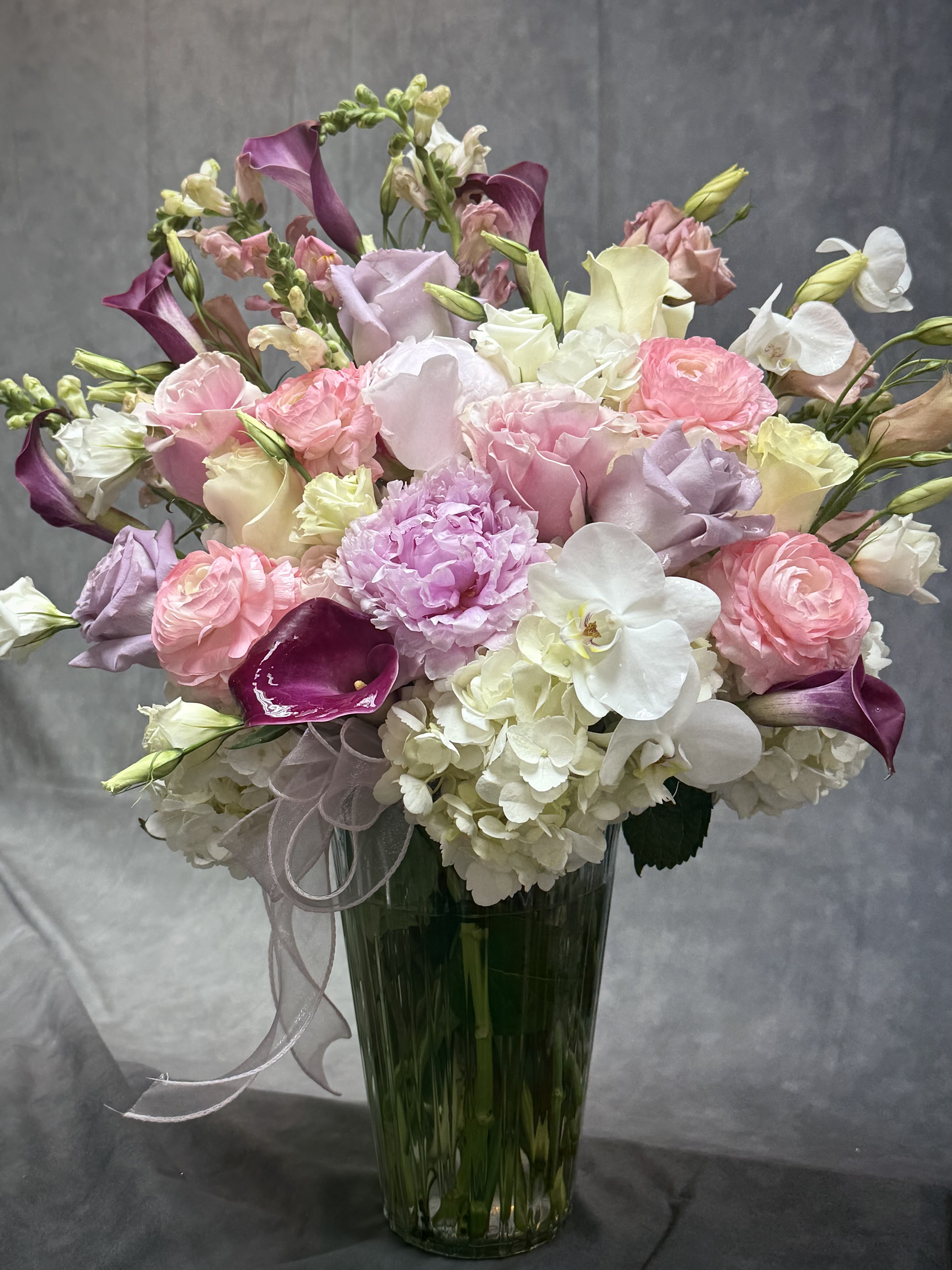 The Luxurious Moment Vase - A breathtaking blend of elegance and charm, The Luxurious Moment Vase features lush hydrangeas, premium roses, delicate orchids, romantic calla lilies, and a stunning peony in soft shades of blush, lavender and ivory. Designed to make every occasion unforgettable, this luxurious arrangement brings beauty, sophistication, and a touch of timeless romance to any space. 