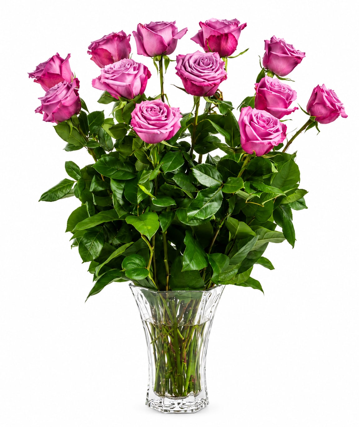 Dozen Long Stemmed Lavender Roses  - A dozen long-stemmed lavender roses arranged in a clear glass vase-think layered, open blooms in soft lavender-pink that read romantic and joyful all at once. This birthday or "just because" bouquet makes the person you're thinking of feel seen: tender, celebrated, and a little bit swoony-perfect for love and romance, a wedding touch, a heartfelt thank you, or even Valentine's Day.  The arrangement features 12 long-stemmed roses with glossy green foliage packed around the stems for a lush, upright silhouette and classic florist finish. The bright lavender-pink petals sit above a simple transparent vase so the color and texture of the blooms take center stage; the overall look is fresh and unfussy, equally at home on a bedside table or a dining-room centerpiece.  Sized to make an impression without overwhelming a room-approximately 25" H x 18" W-this is the kind of bouquet that arrives ready to wow. Minimal care: keep water fresh, trim stems if needed, and enjoy watching her feel genuinely celebrated.