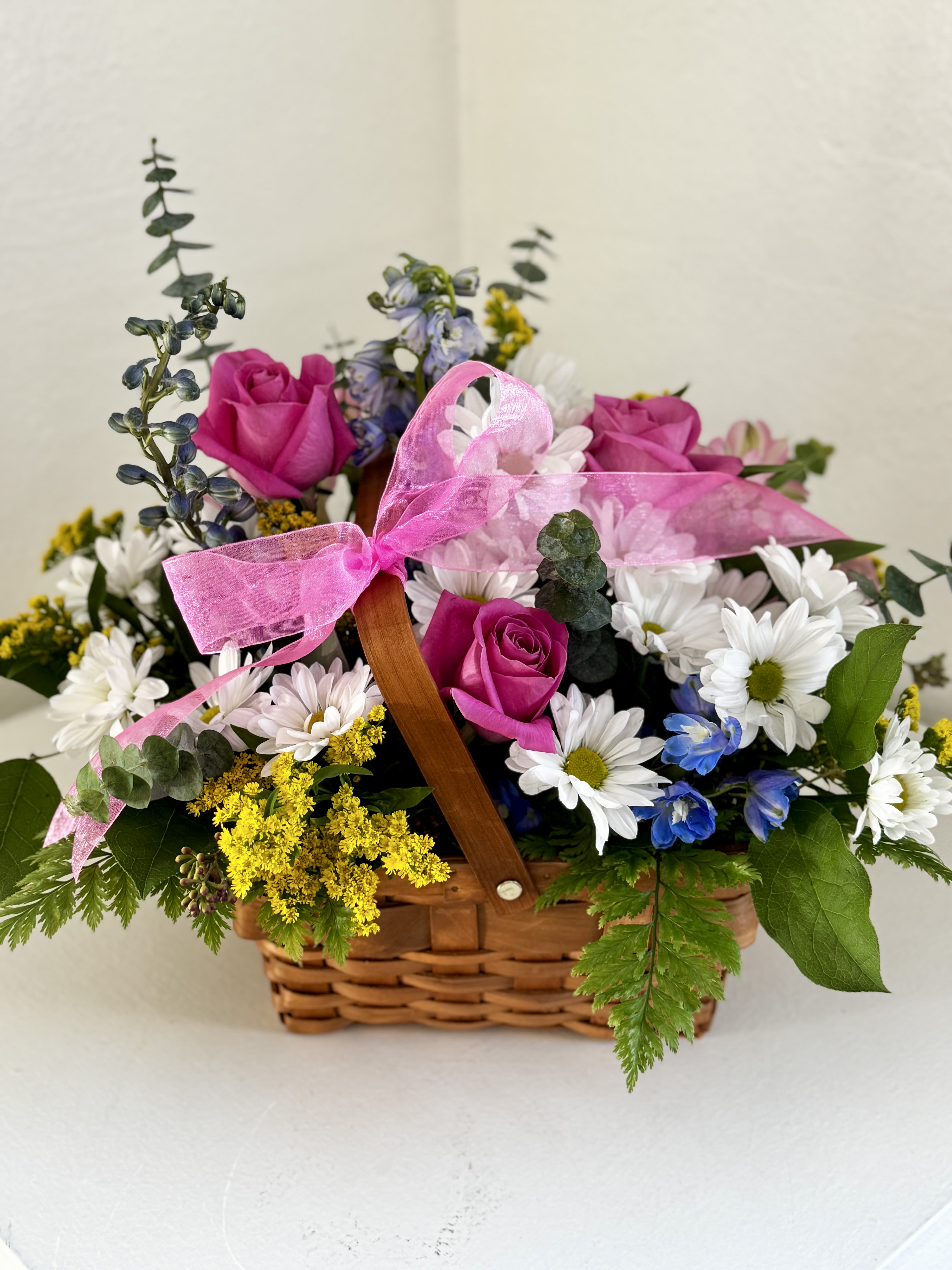 Basket arrangement with pink roses, white daisies, and a pink ribbon