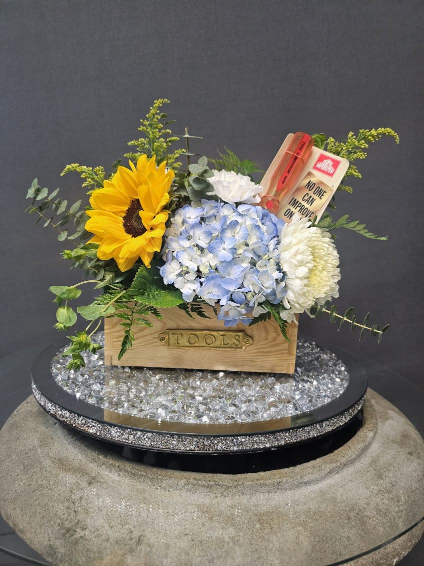 Toolbox Blooms - A bold golden sunflower takes center stage in this cheerful flower arrangement, perfect as a birthday bouquet, thank-you gift, or a just-because surprise. The mix of sunflowers, pale blue hydrangea, white chrysanthemum-like blooms and white carnations reads sunny and uplifting-the kind of bouquet that makes the person you're thinking of smile as soon as it arrives.  