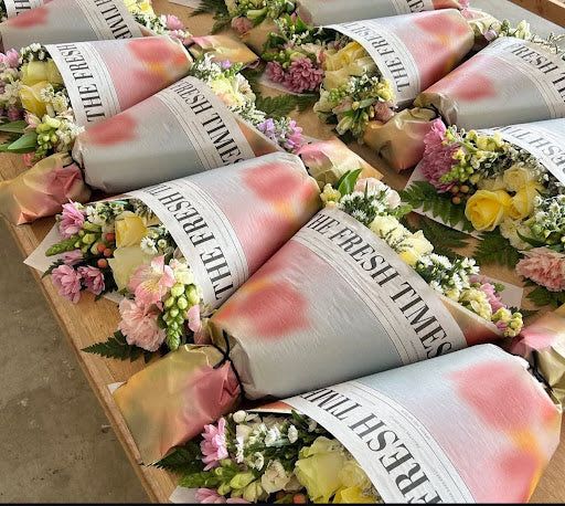 Multiple pastel-wrapped mixed flower bouquets with yellow roses and pink blooms on a wooden table