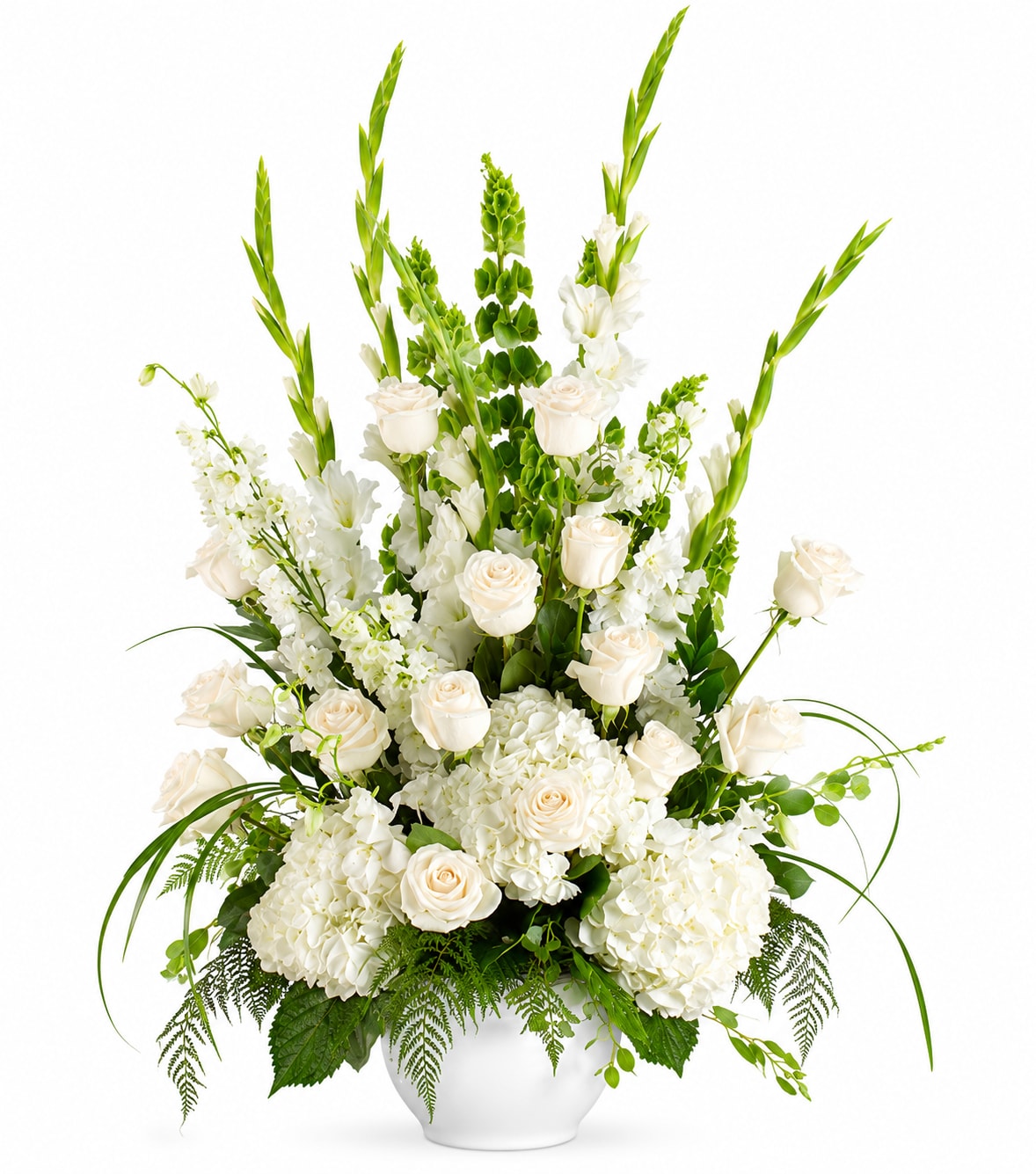 Ivory Hour - Ivory Hour greets the eye with a serene, upright silhouette-the kind of sympathy and funeral flower arrangement that reads as both elegant and quietly consoling. This white sympathy arrangement places roses and clustered hydrangeas at the base for a soft, round foundation while vertical stems-delphinium, bells of Ireland and airy orchids-rise like gentle, green-edged sentinels. The effect is peaceful and refined, the kind of bouquet that helps the person you're thinking of feel seen and soothed.  The palette stays strictly white and green: creamy roses, snow-white hydrangeas, fragrant lilies, delicate orchids and tall delphinium layered with bells of Ireland and light filler blooms for texture and movement. Arranged in a clean white ceramic vase, the composition balances rounded and architectural forms-bloomy mass below, linear accents above-so it looks composed from every angle. Dimensions and stem lengths create a tall, vertical presentation that reads formal without feeling cold.  Perfect for honoring a life or offering quiet support, Ivory Hour sends a message of peace and respect-suitable for memorial services, the family home, or to leave at a graveside where permitted. The ceramic vase arrives ready to display; simple care is to keep water fresh and trim stems if re-cutting is needed. This is the kind of bouquet that helps someone feel comforted rather than overwhelmed.