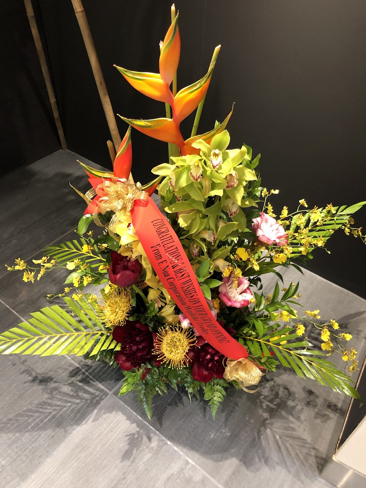 Tropical Anuenue AR2502 - All tropical arrangement with cymbidium orchids, anthuriums and proteas, accented with greenery.