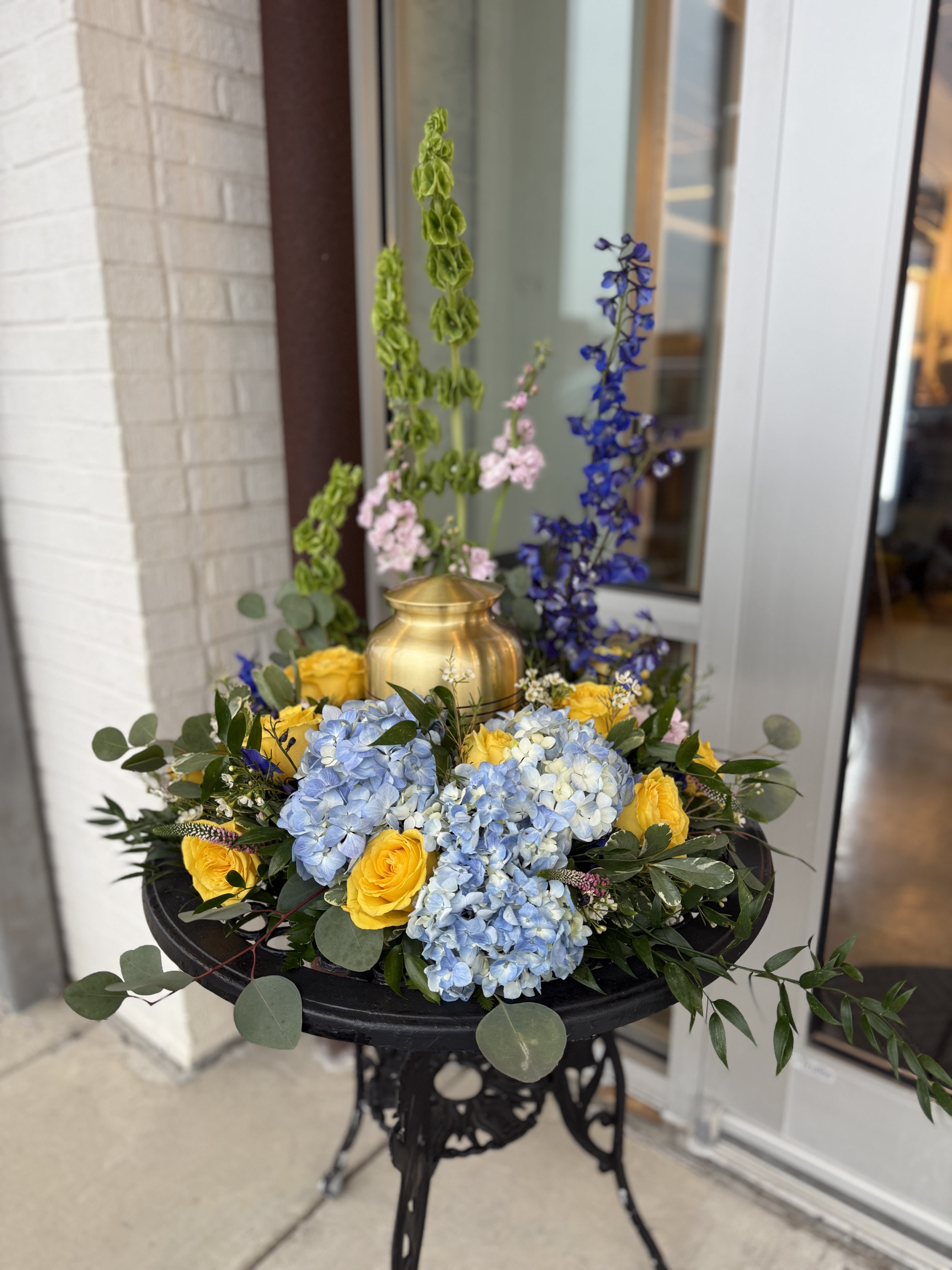 Blue hydrangeas and yellow roses arranged in a gold urn on a black stand