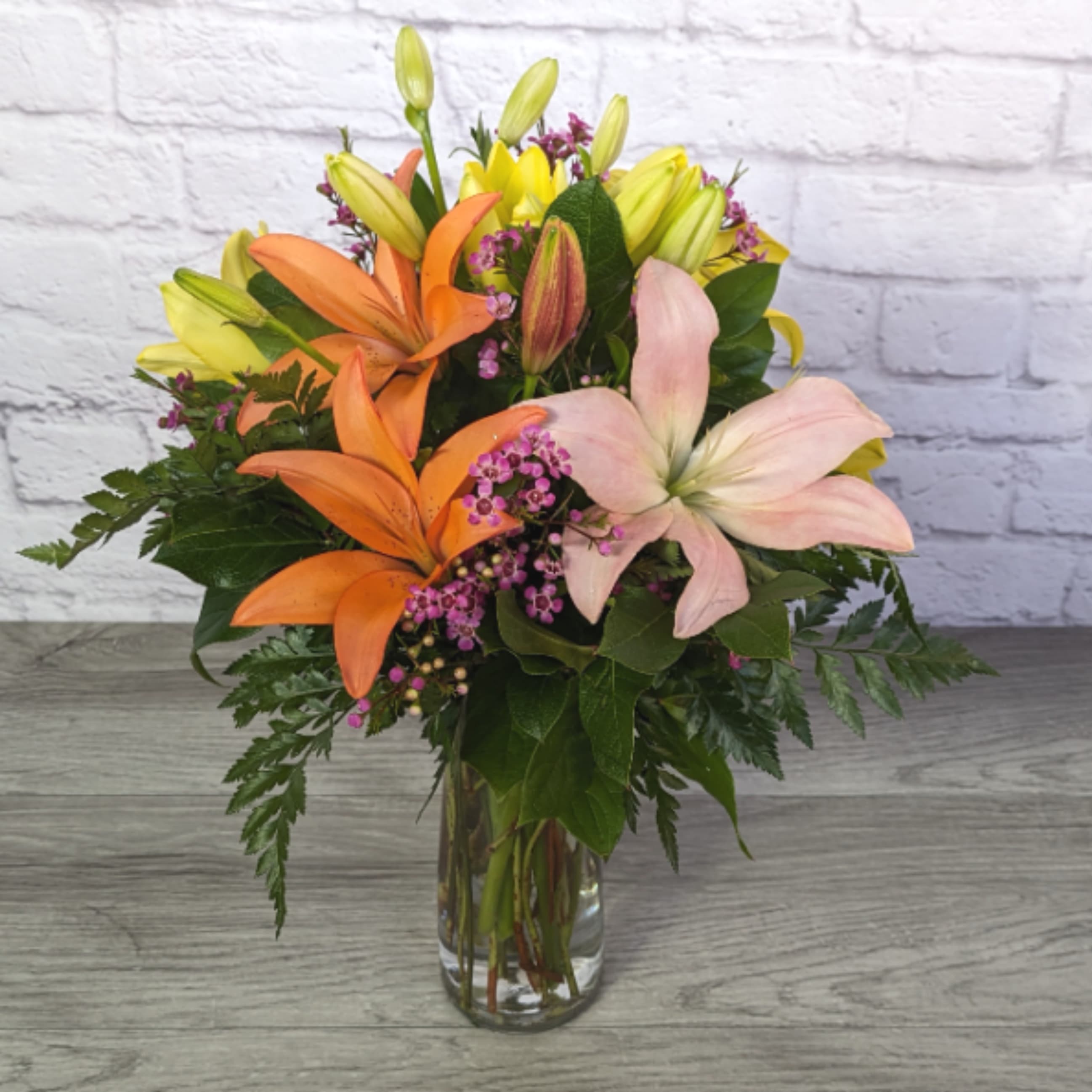 In Love With Lilies - In Love With Lilies is A Ladybug Floral exclusive bouquet. Packed full of Asiatic lilies in mixed colors paired with matching wax flower. Presented in our 9” trio vase.  All Round Orientation 20"H X 14"W  *Lilies may arrive in bud form. With proper care and watering they will open. Some colors may be substituted, however we will maintain the same overall look and feel of the original bouquet.* 