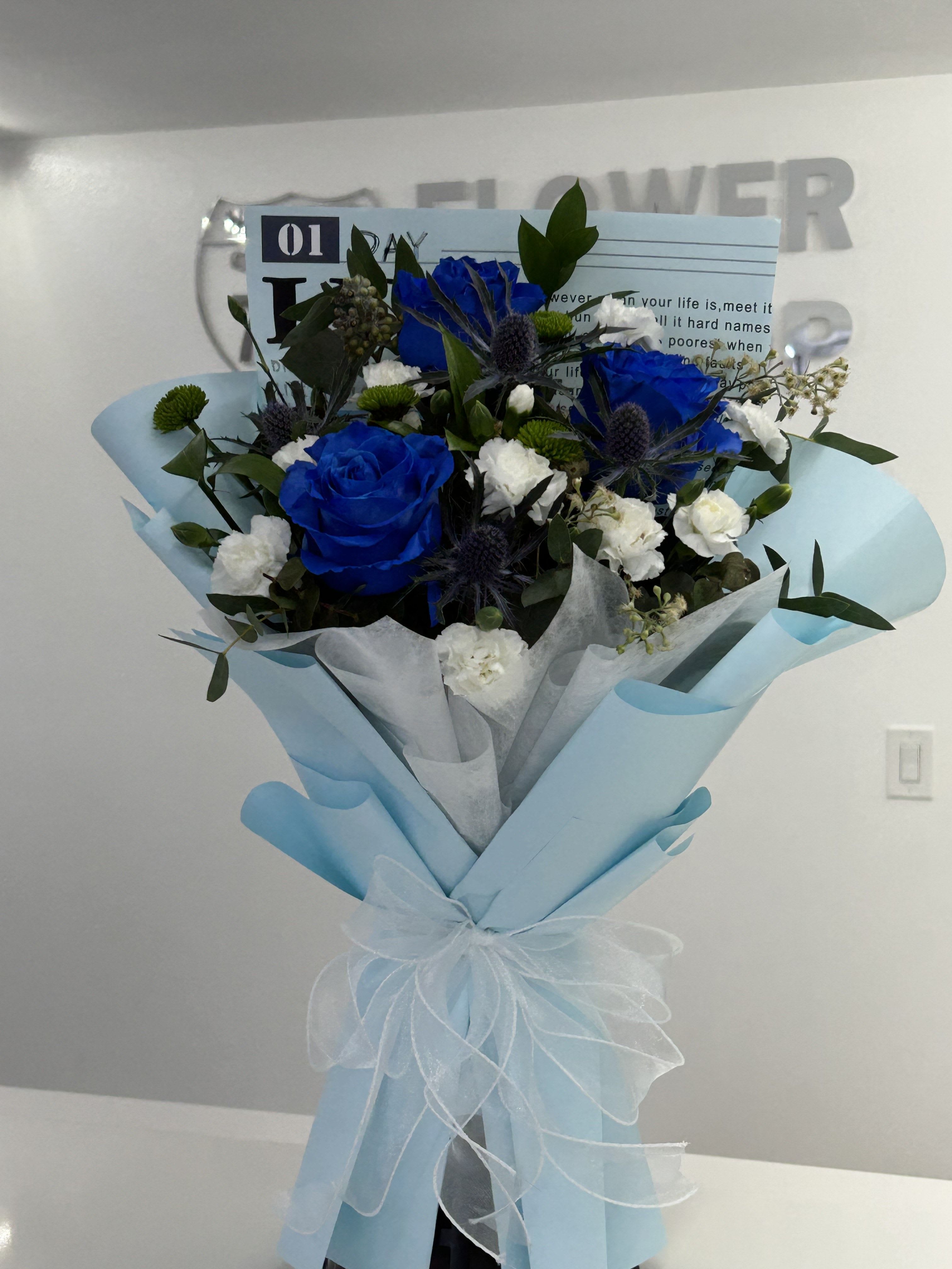Blue Serenity - Elegant, calming, and unforgettable, the Blue Serenity Bouquet features a striking blend of rich blue tones, crisp white accents, and lush greenery, creating a design that is both modern and timeless. Wrapped in soft sky-blue paper and finished with a delicate sheer ribbon, this handcrafted arrangement symbolizes trust, admiration, and heartfelt appreciation. (If some flower colors and/or the vase are not available there will be minor substitutions.)