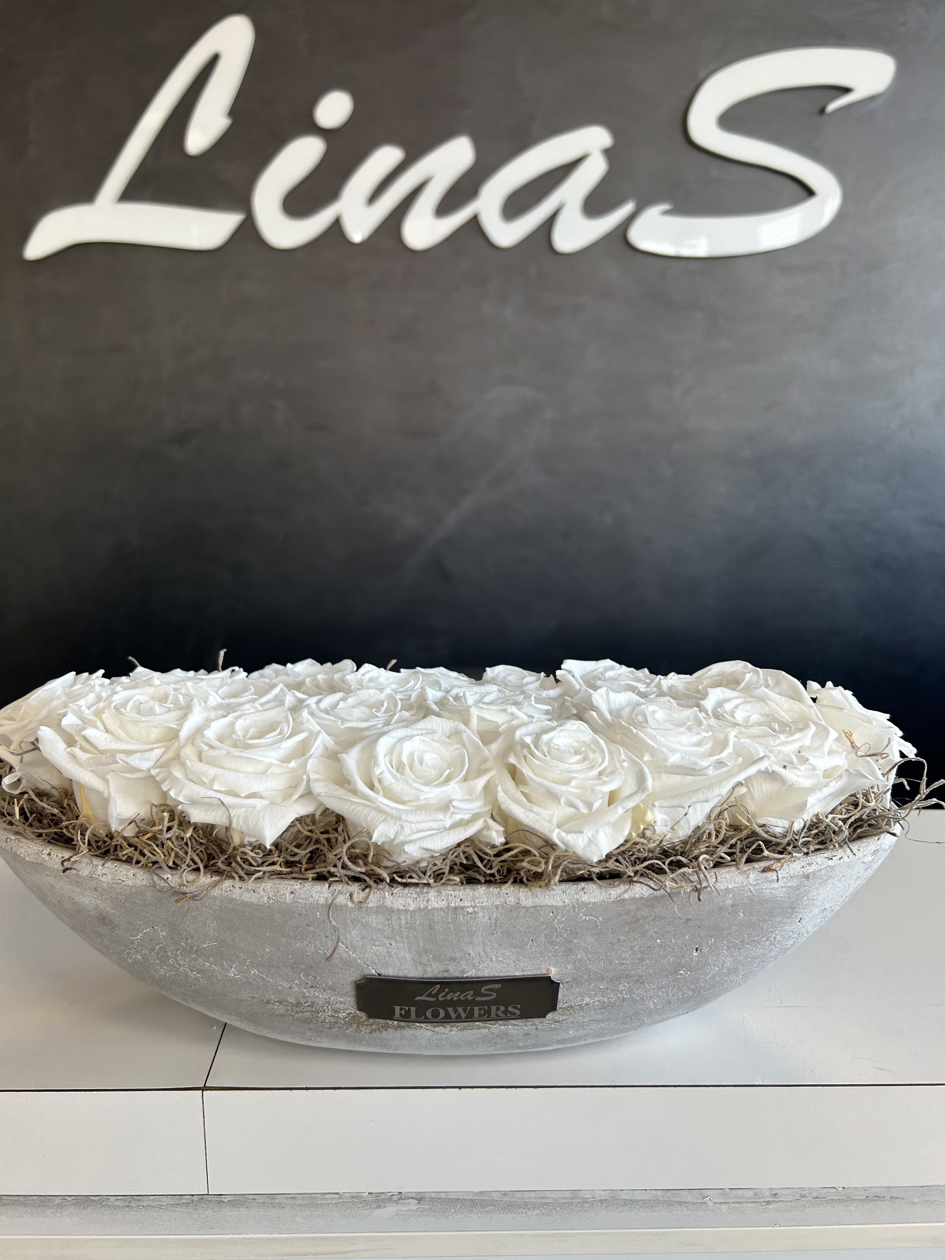 White roses arranged in a shallow gray bowl with dried filler