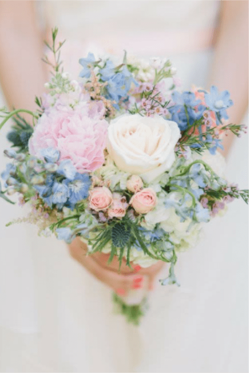 AIRY GARDEN BOUQUET - The bouquet features a white rose, paired with a light pink garden rose, blush pink spray roses, light blue delphiniums, blue blossoms, purple waxflowers, white hydrangea, blue thistles, and wispy filler greens to give it an airy garden-style feel.