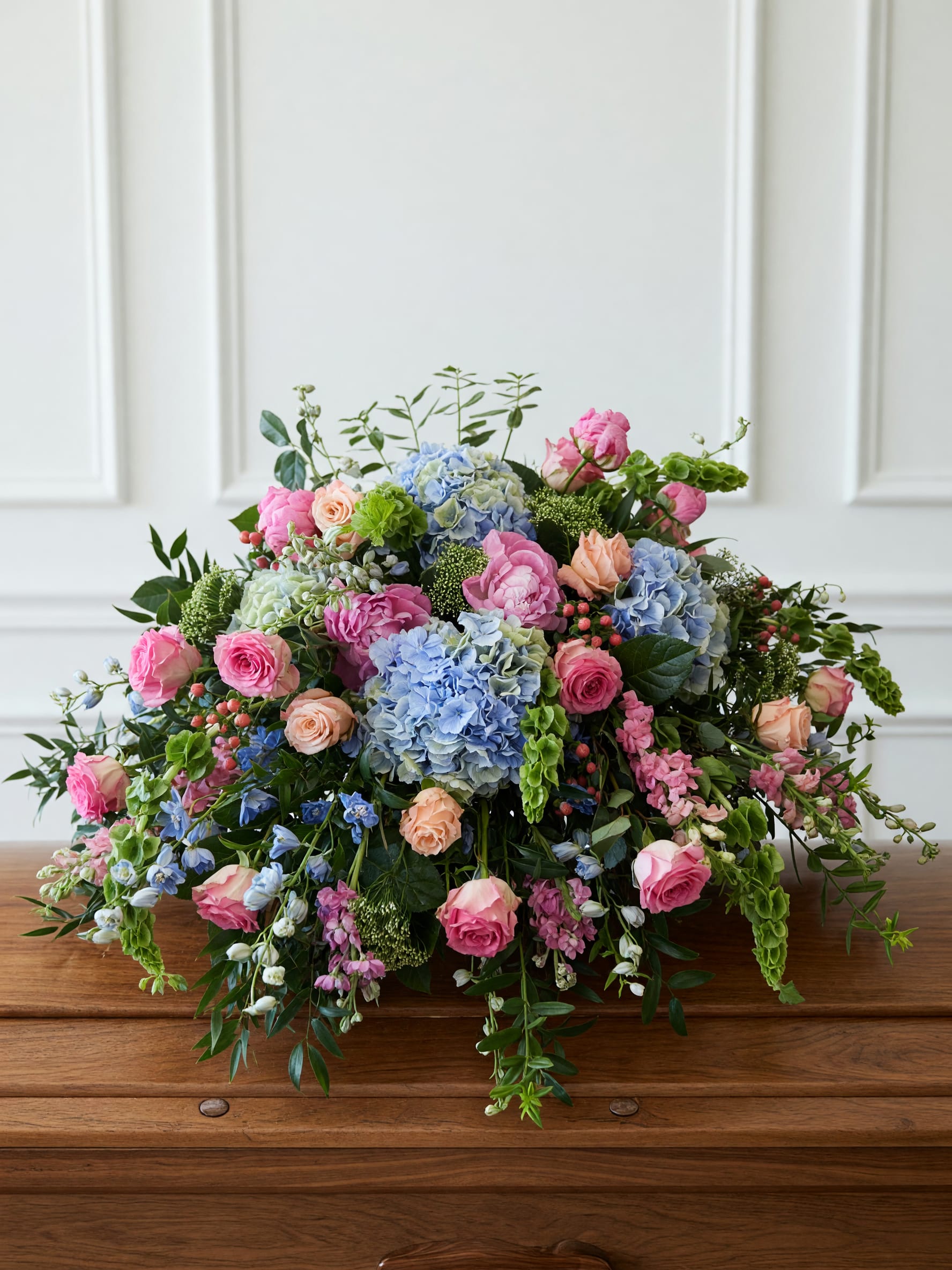 Pastel Garden Casket Cover  - A lush, garden-inspired casket cover designed in soft shades of blue, pink peaches and fresh greens. Designed with seasonal blooms, this elegant tribute creates a stunning expression of love and remembrance.  Appropriate for an open or closed casket. Please call to shop to discuss specific designs, flowers or alternative color palettes.  Approx. size 42" L x 24" W x 20" H