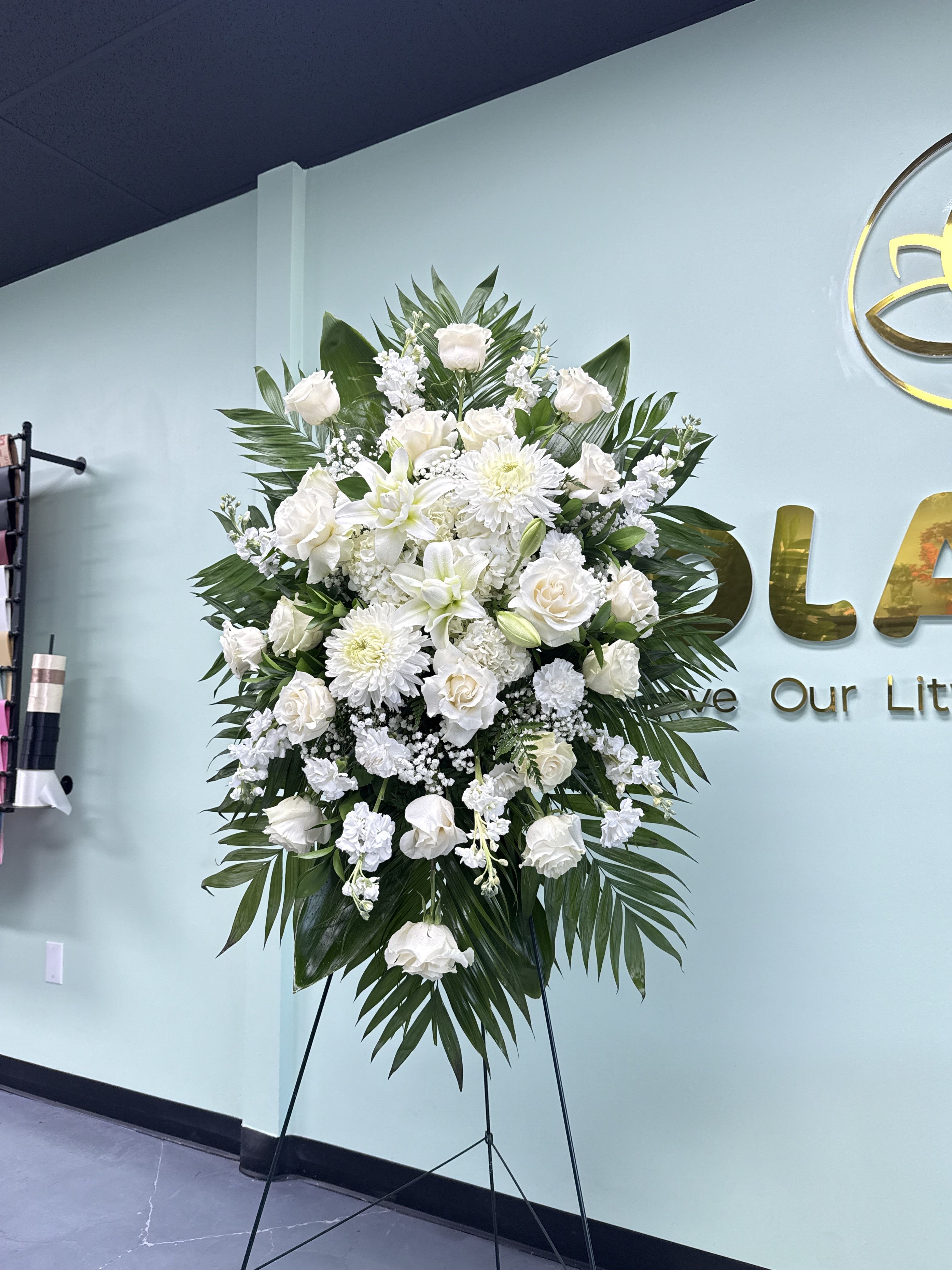 Sympathy - Traditional 02 - White roses, lilies, chrysanthemums, carnations and stock arranged with palm fronds on a black easel - a tall, serene standing spray in white and green for sympathy and memorials.