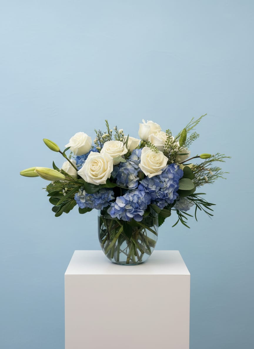 Something Blue - A stunning collection of crisp white roses, lush blue hydrangea, elegant lilies, and premium greenery arranged in a classic glass vase. Inspired by the timeless tradition of “something blue,” this design symbolizes love, hope, and lasting happiness. With its soft textures and sophisticated color palette, it’s a beautiful choice for celebrations, sympathy, or simply brightening someone’s day.