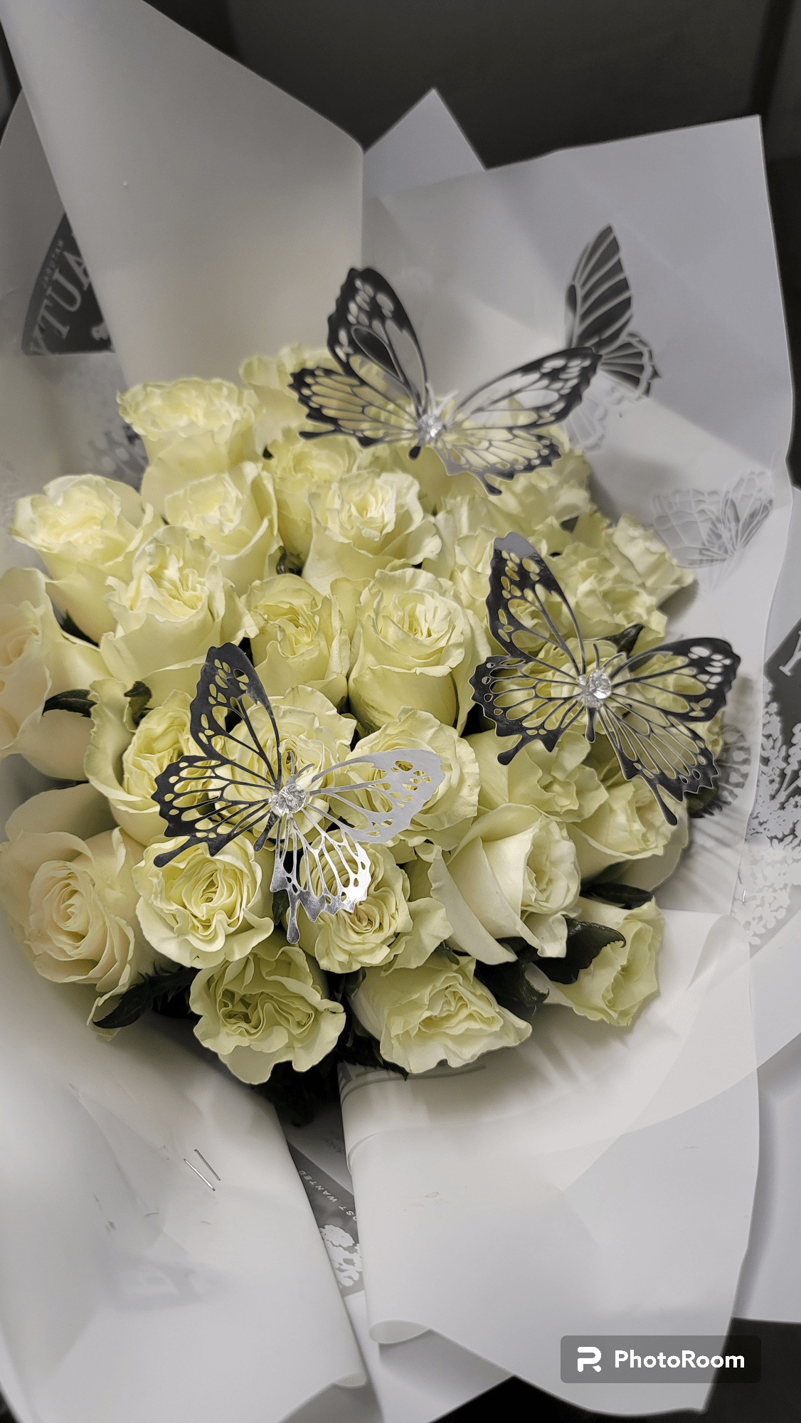 Sandy - A cluster of pale yellow roses gathered into a rounded hand-tied bouquet makes a quietly joyful statement - the perfect birthday bouquet or anniversary flowers to make the person you're thinking of feel gently celebrated. The soft yellow tones read as cheerful and slightly romantic, while black-and-white butterfly picks add a whimsical, memorable accent that elevates the arrangement beyond an everyday posy.  Tightly clustered roses are wrapped in crisp white paper for a clean, formal presentation that's easy to carry or place in a vase at home. The compact, rounded shape keeps the focus on the blooms' petal texture and warm color; the decorative butterfly picks introduce contrast and personality. Choose this arrangement for birthdays, small celebrations, or to send a heartfelt "thinking of you" - it arrives ready to present and will brighten a bedside table or dining room centerpiece.