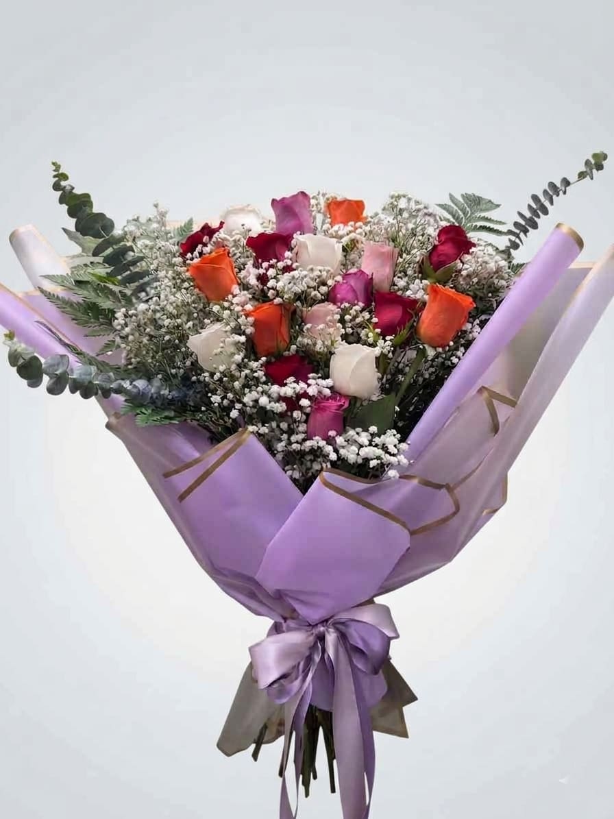 Floral Luxe by The Flower Spot™ - A lavish cluster of mixed-color roses creates an immediate sense of celebration - perfect as a birthday bouquet, Mother's Day gift, anniversary roses, or a heartfelt thank-you arrangement. Floral Luxe by The Flower Spot™ reads lush and romantic at first glance: tightly gathered roses in red, pink, lavender, white, and peach make a joyful color story that will make the person you're thinking of feel truly cherished.  The arrangement pairs those curated roses with delicate white filler flowers and fresh greenery for texture and depth, wrapped in soft pastel decorative paper and finished with a satin ribbon and a gift tag for an elegant presentation. The layered composition feels full without being crowded, offering varied heights and petal textures that catch the light and fragrance of the roses.  Give this to a mother, partner, friend, or colleague to mark a meaningful moment - it's the kind of bouquet that makes someone feel seen and celebrated. Arrives ready to display in the wrapping; trim the stems and place in fresh water for best longevity.