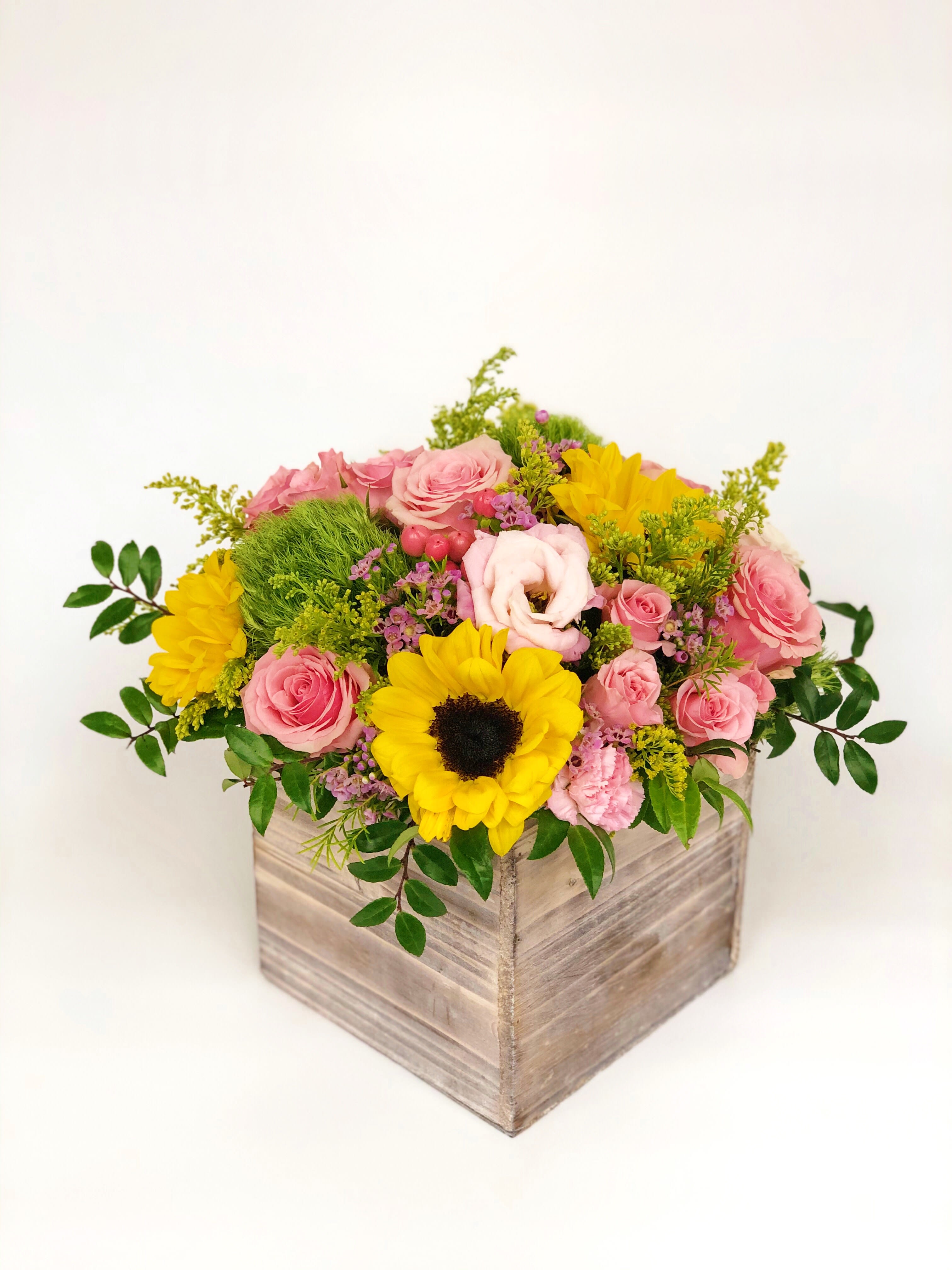 Low wooden box arrangement with yellow sunflowers and pink roses accented by green and purple blooms