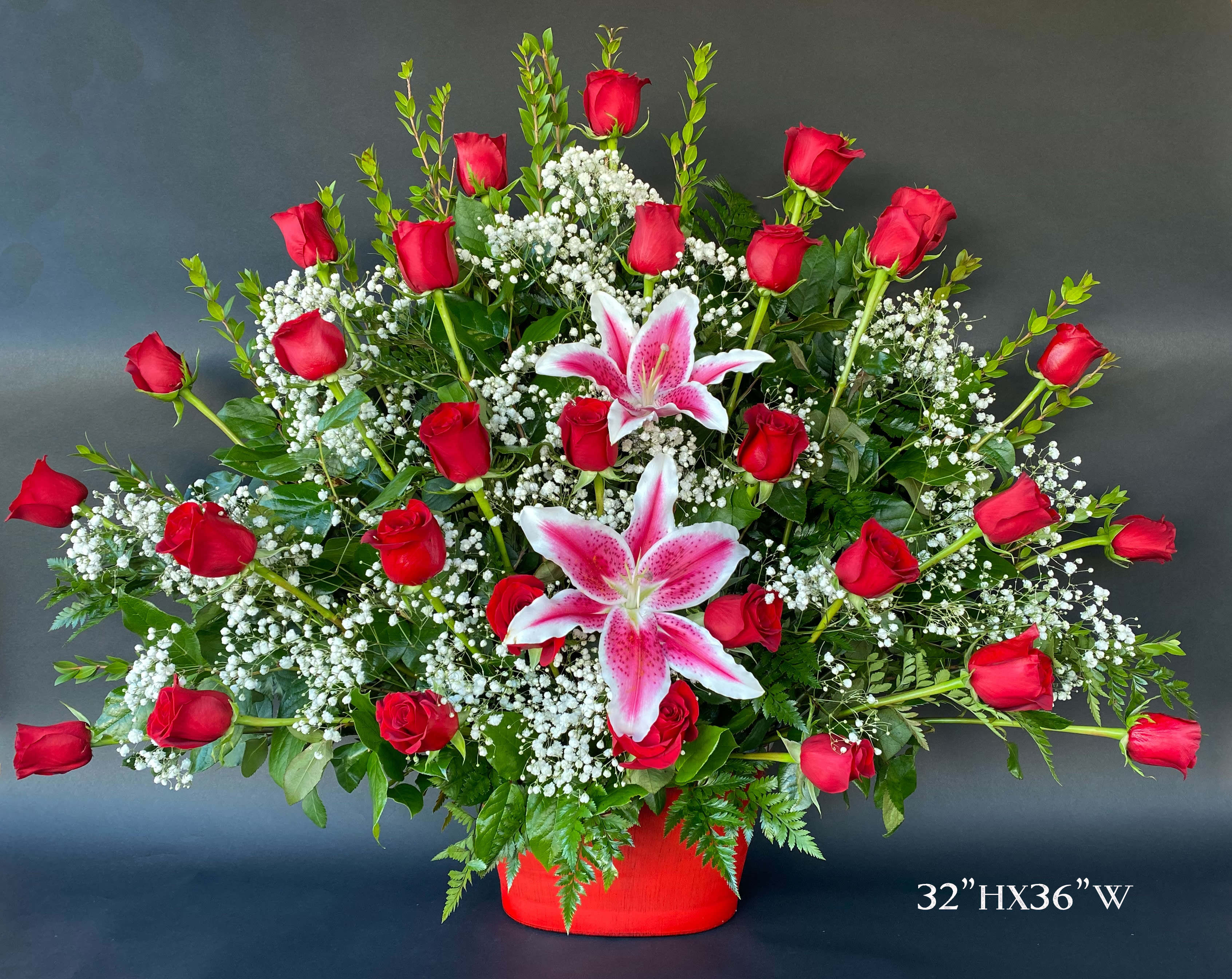 Large arrangement of red roses and pink lilies in a red container
