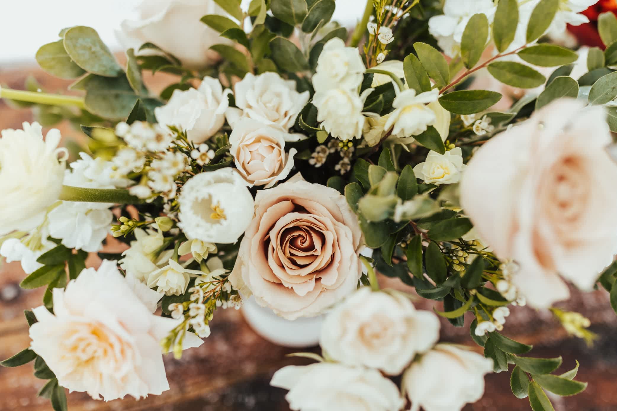 Arrangement of blush roses and white flowers in a white vase on a wooden surface