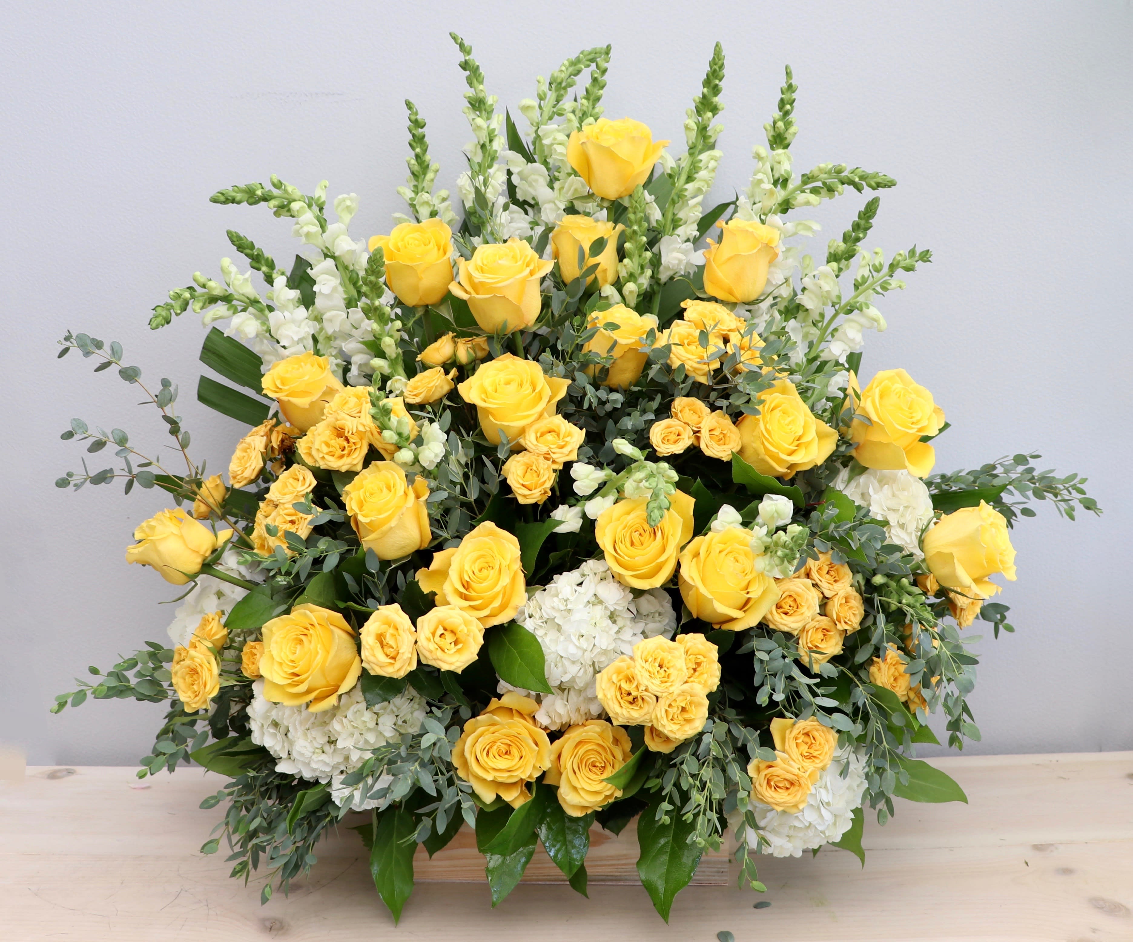 Large arrangement of yellow roses, yellow spray roses, white hydrangeas, and white snapdragons in a wooden container
