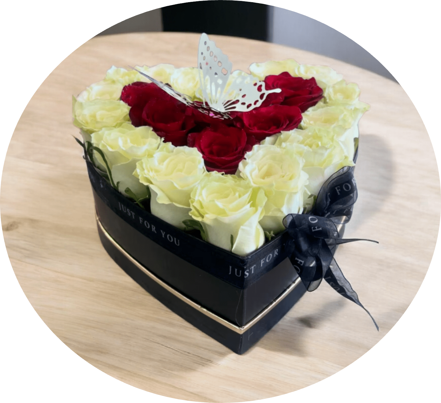 Andalucia - A compact heart-shaped arrangement of roses designed to make the person you're thinking of feel truly cherished. This heart-shaped gift box bouquet reads romantic at a glance-deep red roses clustered in a dense center framed by a border of pale cream-white roses-so it's ideal for anniversaries, Valentine's Day, or any love-themed occasion when you want her to feel celebrated.  The roses are tightly packed for a lush, velvety texture; a black box and matching black ribbon give the composition an elegant, modern contrast to the red and cream petals. A delicate decorative butterfly topper rises from the center, adding a light, whimsical accent to the otherwise bold palette and reinforcing the gift-like presentation.  Perfect for hand delivery or a special surprise at home, this boxed rose arrangement arrives ready to display with minimal fuss. The compact size makes it easy to set on a bedside table or desk where the recipient will see it often and remember your thoughtfulness.