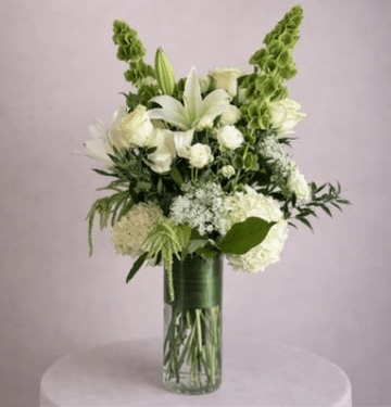 White lilies and hydrangeas in a tall glass vase with green accents