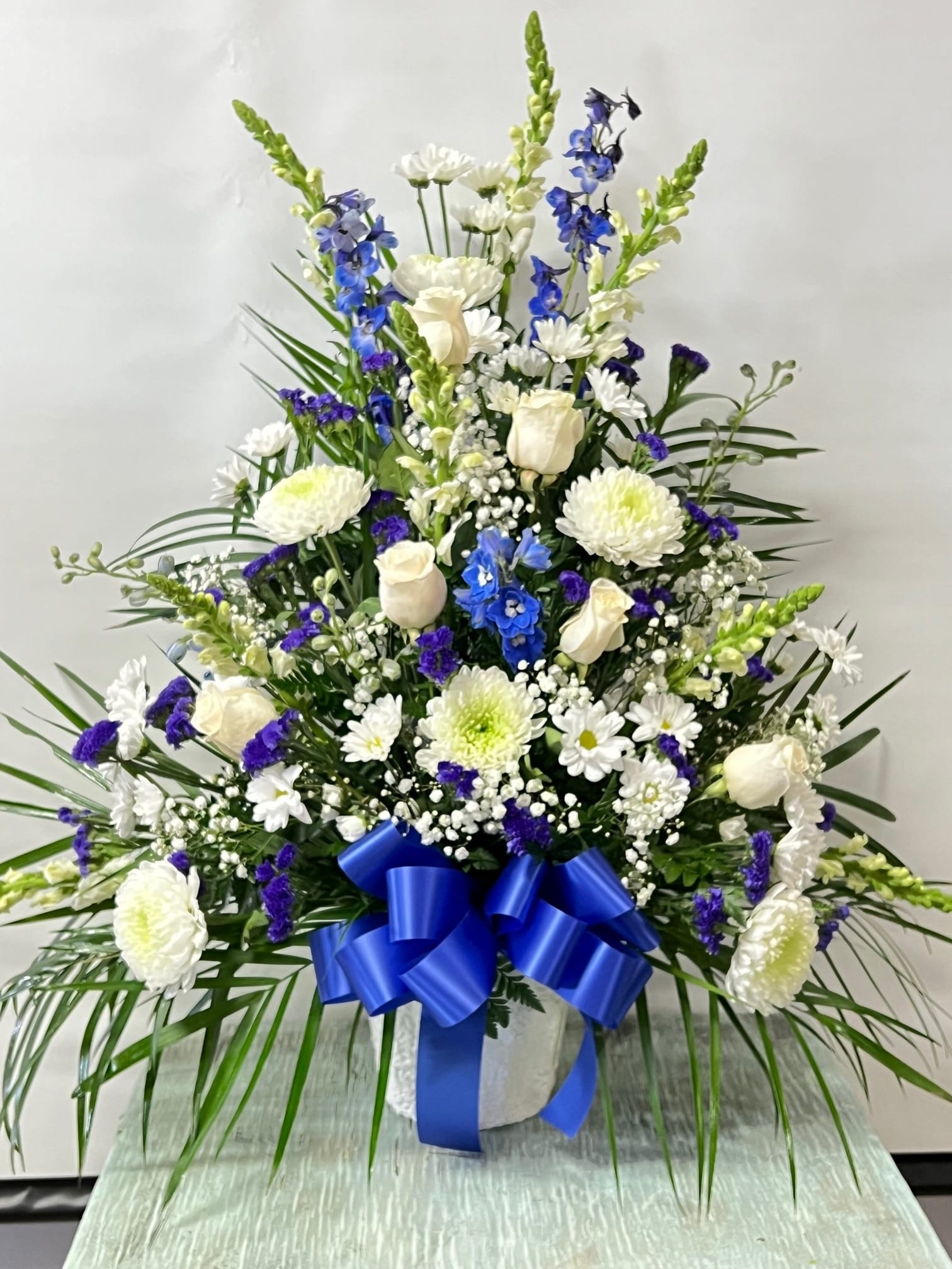 Tall white and blue floral arrangement with a blue ribbon in a vase
