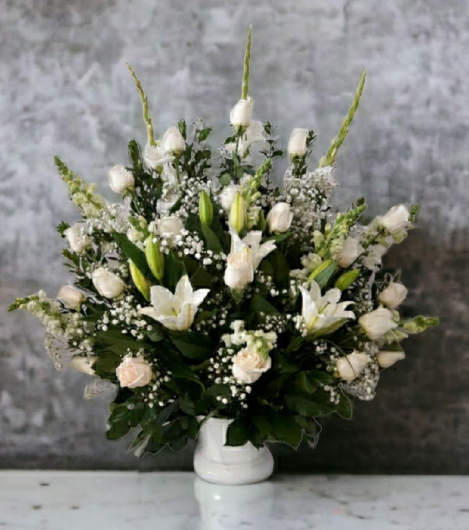 White floral arrangement in a white vase with lilies and roses