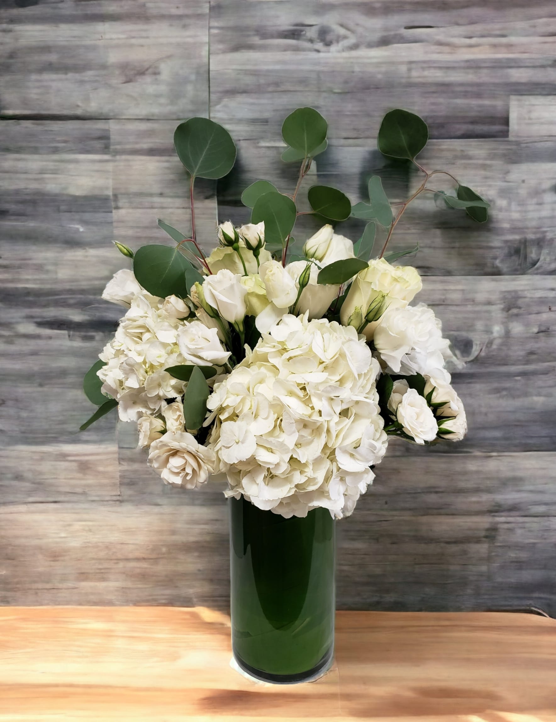 White flowers arranged in a tall green vase with round eucalyptus stems