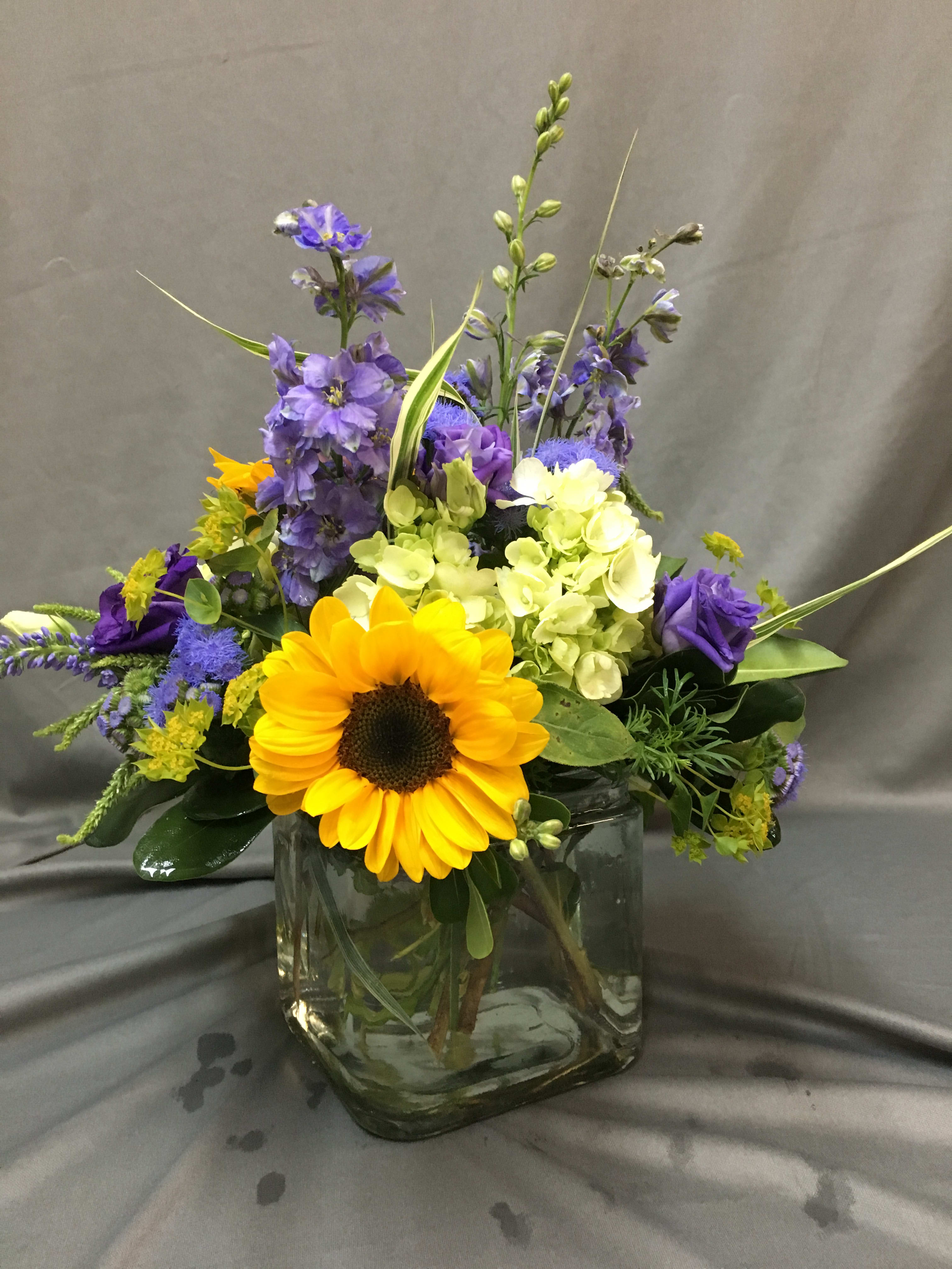 Mixed bouquet with a sunflower and purple blooms in a glass vase