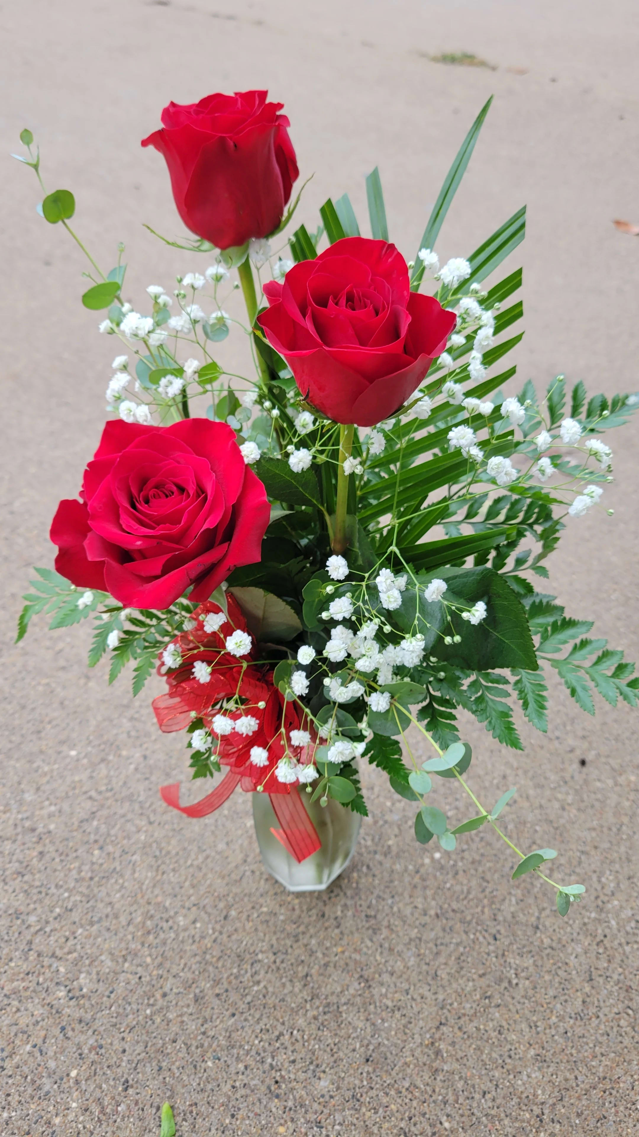 Three red roses in a clear vase with white baby's breath