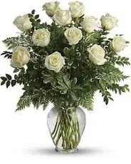 joy of roses  - A cluster of soft ivory roses set among abundant mixed greenery creates a calm, classic bouquet - perfect as a white rose arrangement for sympathy, a wedding accent, or a thoughtful thank-you gift. The rounded silhouette and understated palette give the recipient a sense of quiet elegance and comfort, the kind of arrangement that makes someone feel genuinely seen and cared for.  The arrangement features white roses gathered tightly in a clear glass vase, the creamy petals contrasting with darker, textured foliage for depth and a fresh, natural feel. The vase keeps the design clean and modern while the plentiful greenery gives it a full, garden-fresh presence that works well on a dining table, bedside, or entry console.  Ideal for sending condolences, celebrating a wedding, or saying "I'm thinking of you," this arrangement arrives ready to display. Easy-care and classic in style, it suits recipients who appreciate timeless floral beauty; if you'd like sizing or delivery options, please select your preferred vase size and delivery date at checkout.