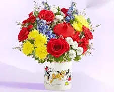  micky mouse &amp; friends cookie jar - Bright, playful and full of cartoon charm, this flower arrangement makes an immediate smile-worthy gift for a birthday, congratulations, or just because. The bouquet-style floral arrangement and the Mickey Mouse-themed ceramic cookie jar vase announce a lighthearted, kid-friendly celebration - the kind of present that will make the person you're thinking of feel seen and delighted.  A dense, rounded mix of red roses, bright yellow daisy-like blooms, small blue flowers and white accents creates a layered, colorful composition that reads cheerful rather than formal. The flowers are arranged tightly for a full silhouette that holds its shape, with the white ceramic vase decorated in Mickey Mouse graphics adding a whimsical keepsake element. Colors include vibrant red, sunny yellow, touches of blue and crisp white for a lively, balanced palette.  Perfect for a child's party, a Disney fan, or anyone who appreciates a nostalgic, fun gift, this arrangement arrives ready to display - the jar can be reused as a cookie jar or decorative piece after the flowers are enjoyed. For best longevity, change the water every couple of days and trim stems slightly when refreshing; available in the pictured design for a bright, celebratory presentation.