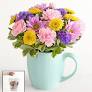 muggable bouquet - A pocket-sized cluster of pastel chrysanthemums and daisies arranged in a light blue ceramic mug makes this flower arrangement a cheerful everyday gift - perfect as a birthday bouquet, a thank-you gesture, or a just-because surprise. The rounded, compact shape reads as friendly and effortless, so the person you're thinking of will feel noticed and brightened without fuss.  Soft pink, sunny yellow, lavender and fresh green tones are packed closely together to create a plush, mixed-bouquet look that feels full despite its small scale. The arrangement sits in a sturdy ceramic mug that doubles as a keepsake; the tight, domed styling keeps stems neat and makes the display easy to place on a desk, bedside table, or kitchen counter.  Choose this muggable bouquet when you want to say "I'm thinking of you" in a casual, delightful way - ideal for coworkers, neighbors, or friends who appreciate simple cheer. No complicated care is required: keep the flowers in a cool spot away from direct sunlight and refresh the water every couple of days to extend the life of the blooms.