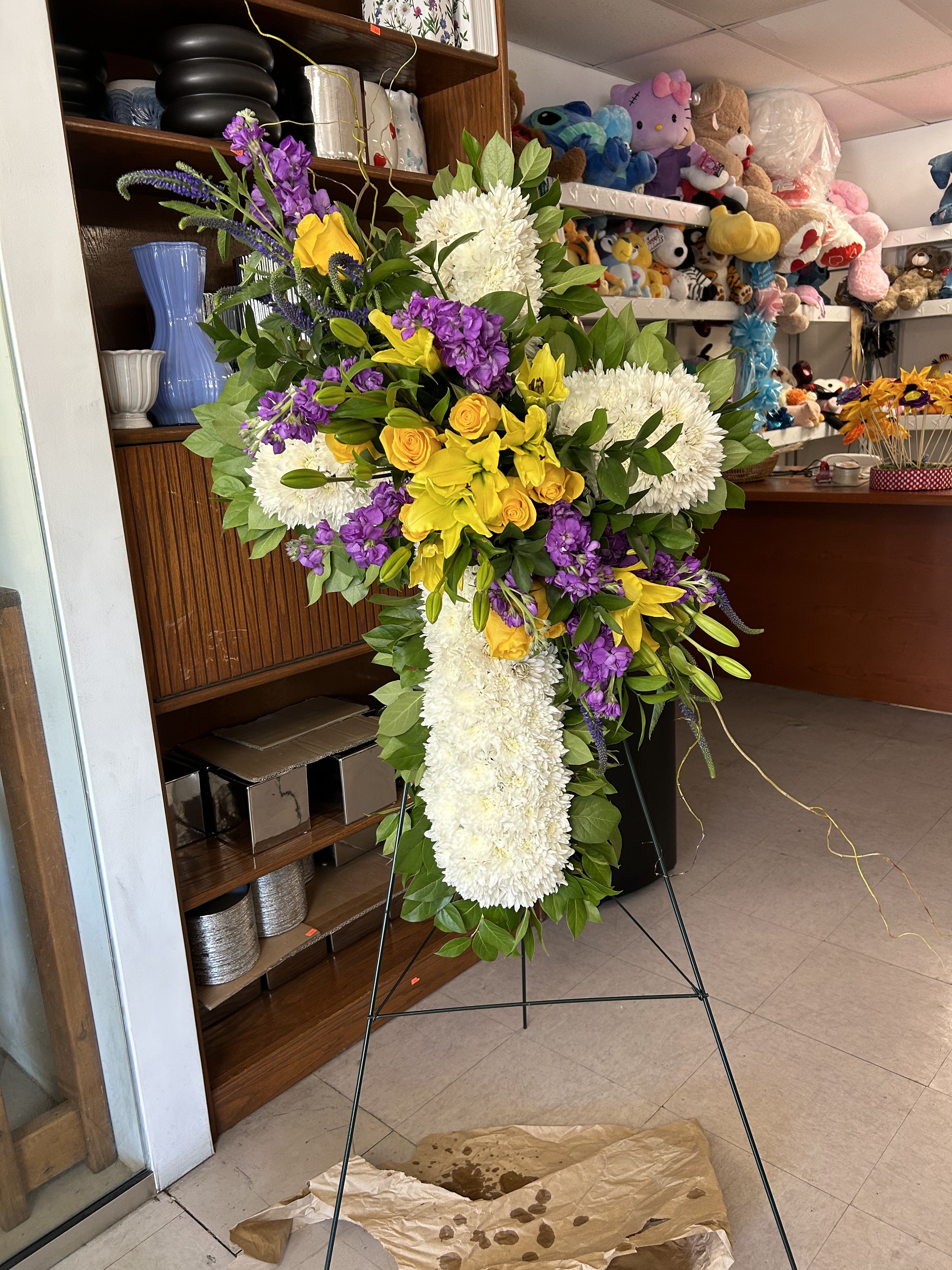 Standing floral cross with white chrysanthemums, yellow roses, and purple flowers