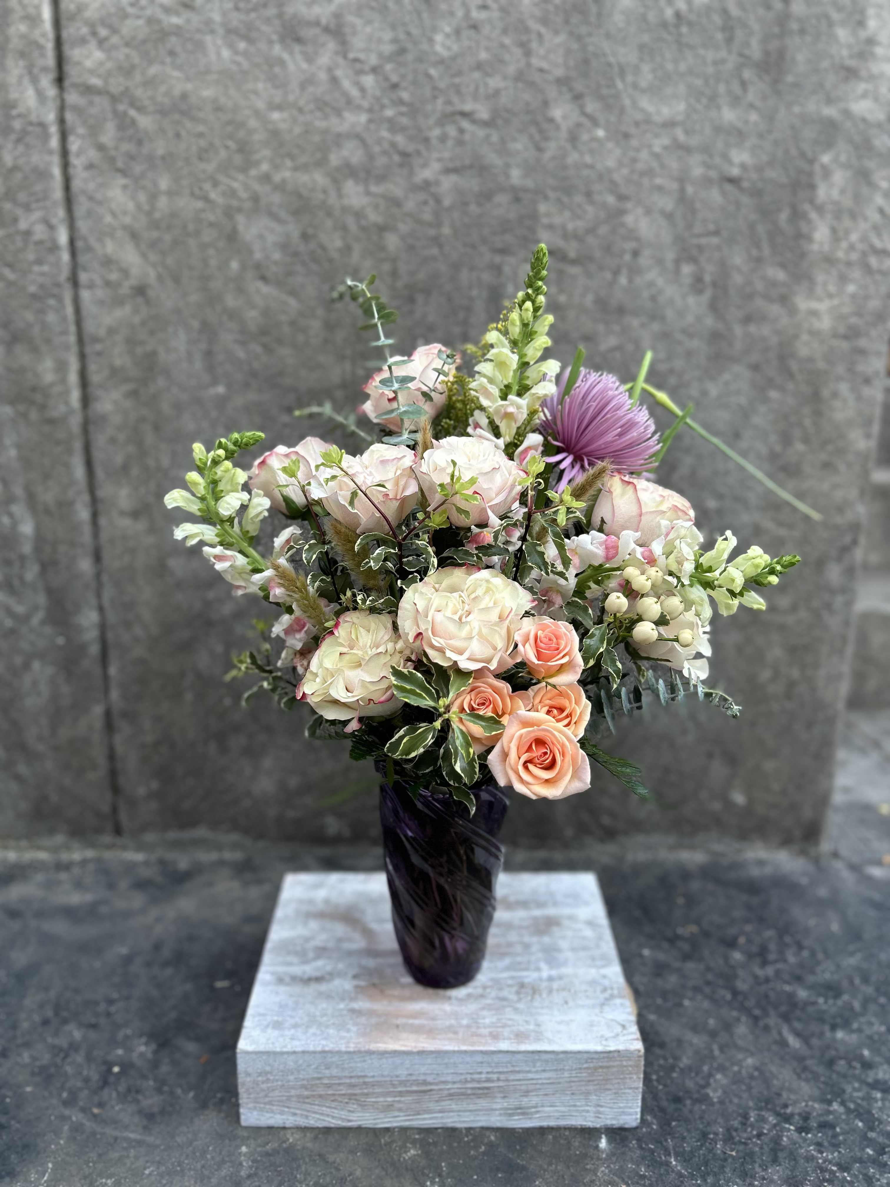 Apple Blossom - Soft colors, frilly roses, snapdragons, spray roses, chrysanthemums, pretty foliages, eucalyptus, in a purple swirl vase.    *Reasonable substitutions may be made due to floral availability. Will have similar look and feel.