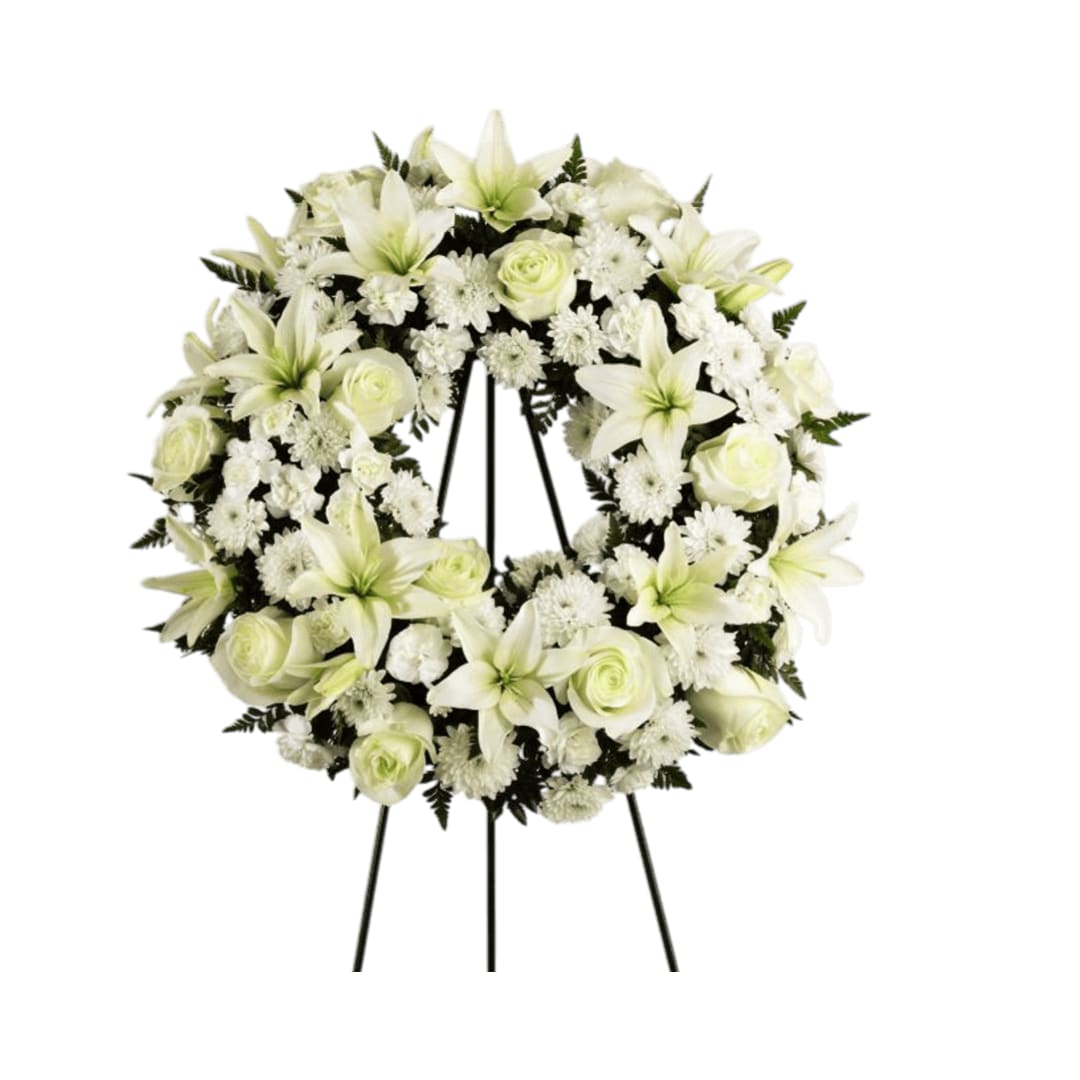 Treasure Tribute Wreath - Treasured Tribute Wreath offers peaceful wishes of  heartfelt sympathy with each delicate bloom. Bright white roses, Asiatic  lilies, mini carnations and cushion poms are beautifully arranged to  form an elegant accented with lush and vibrant greens. Displayed on a  wire easel, this gorgeous tribute is a wonderful symbol of eternal life  and sweet serenity. Approximately 22 inches in diameter. 
