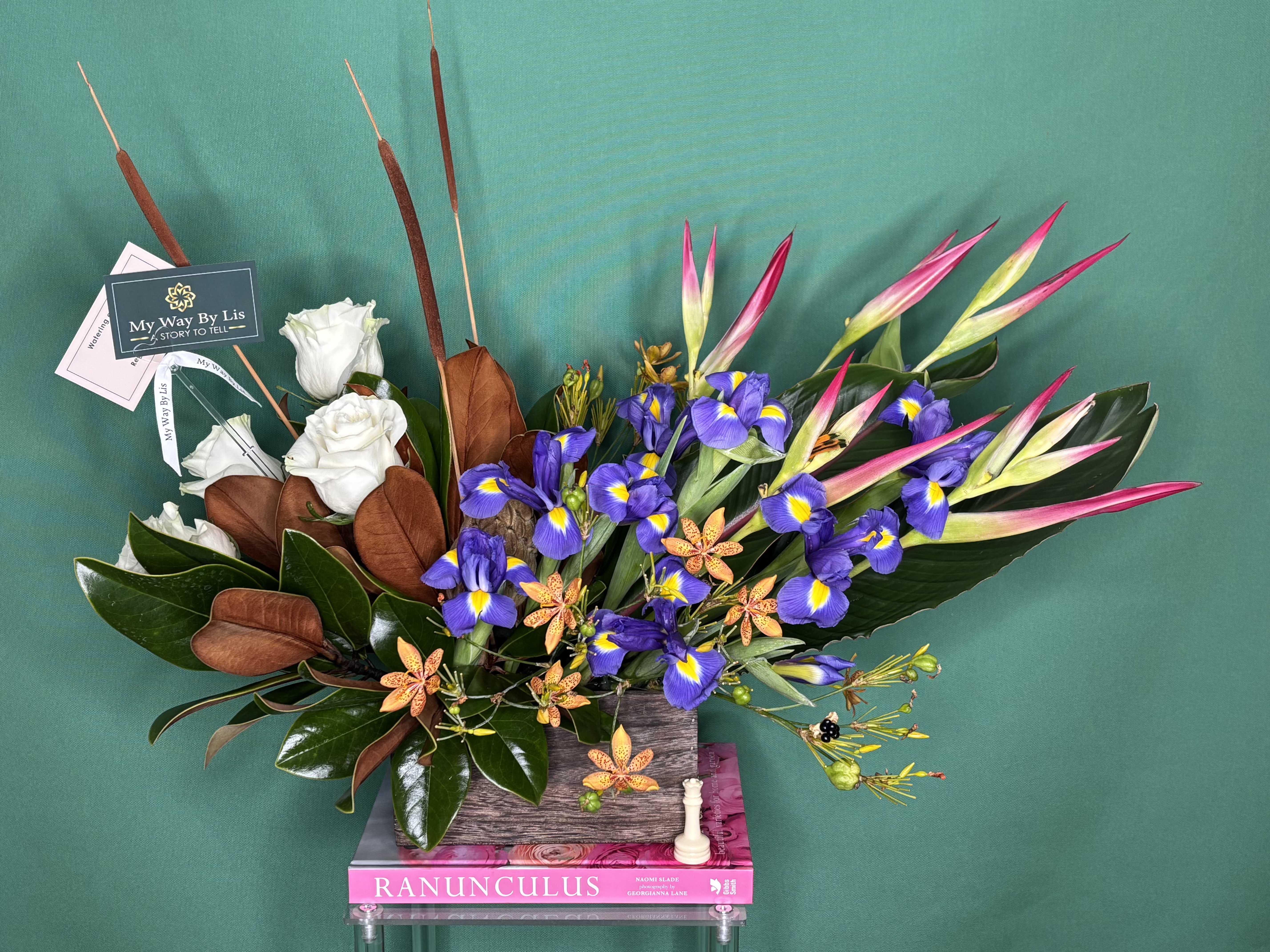 Arrangement of white roses, purple irises, and pink tropical blooms in a rectangular vase