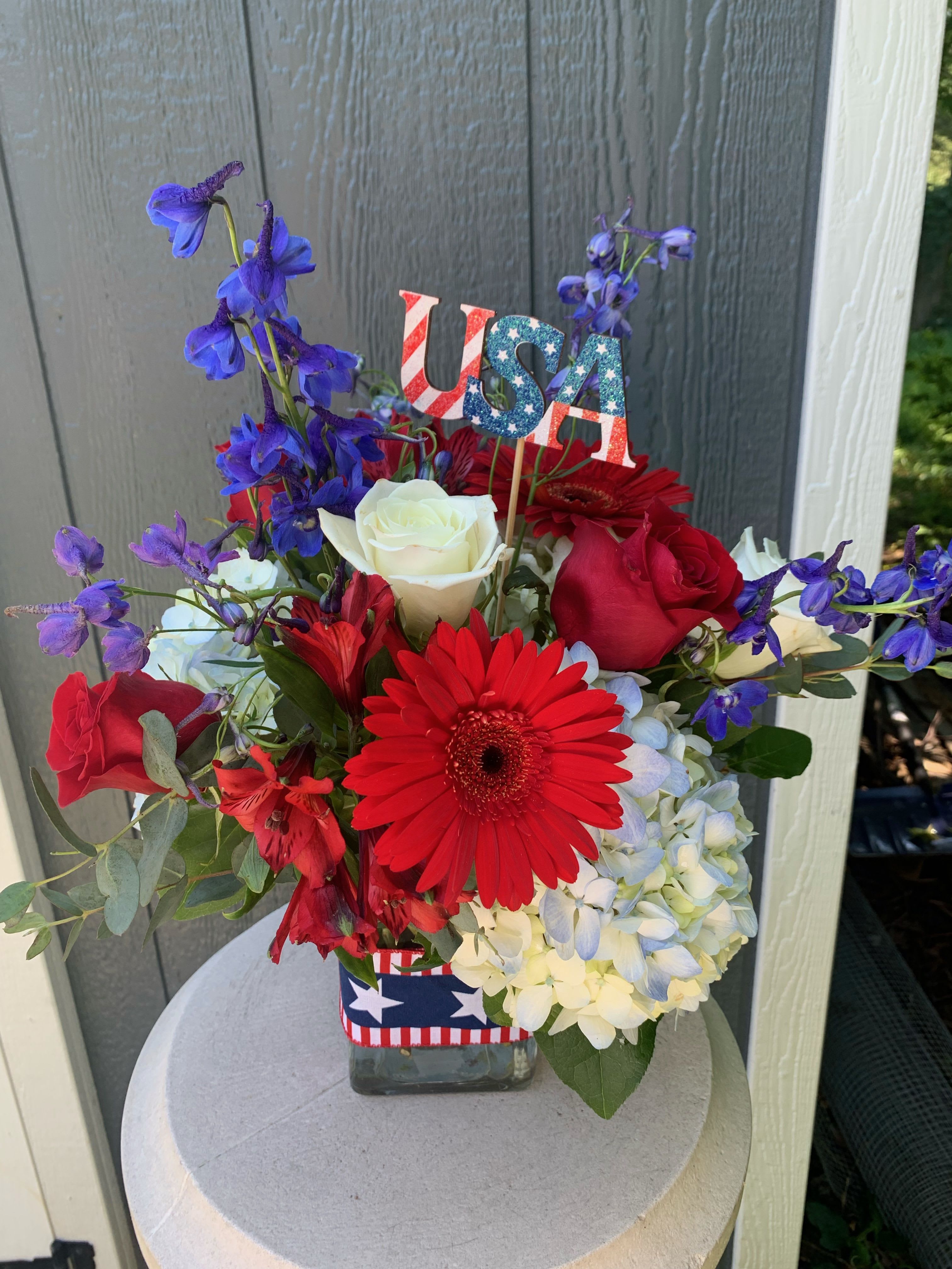 Red, white, and blue flower arrangement in a glass vase with a USA pick