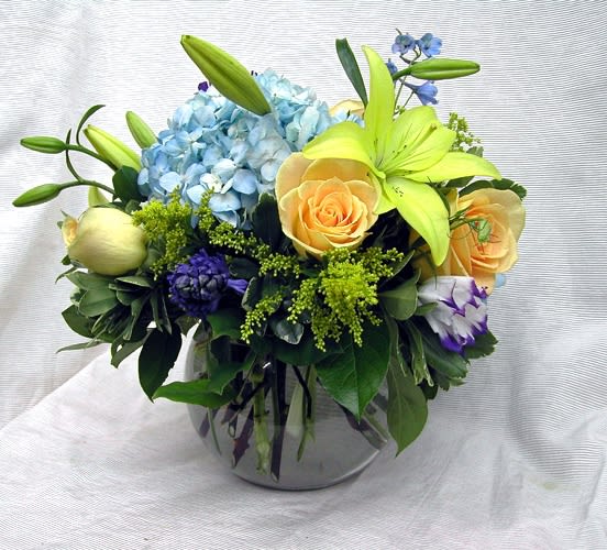 Mixed bouquet with blue hydrangea, yellow lilies, and peach roses in a glass vase