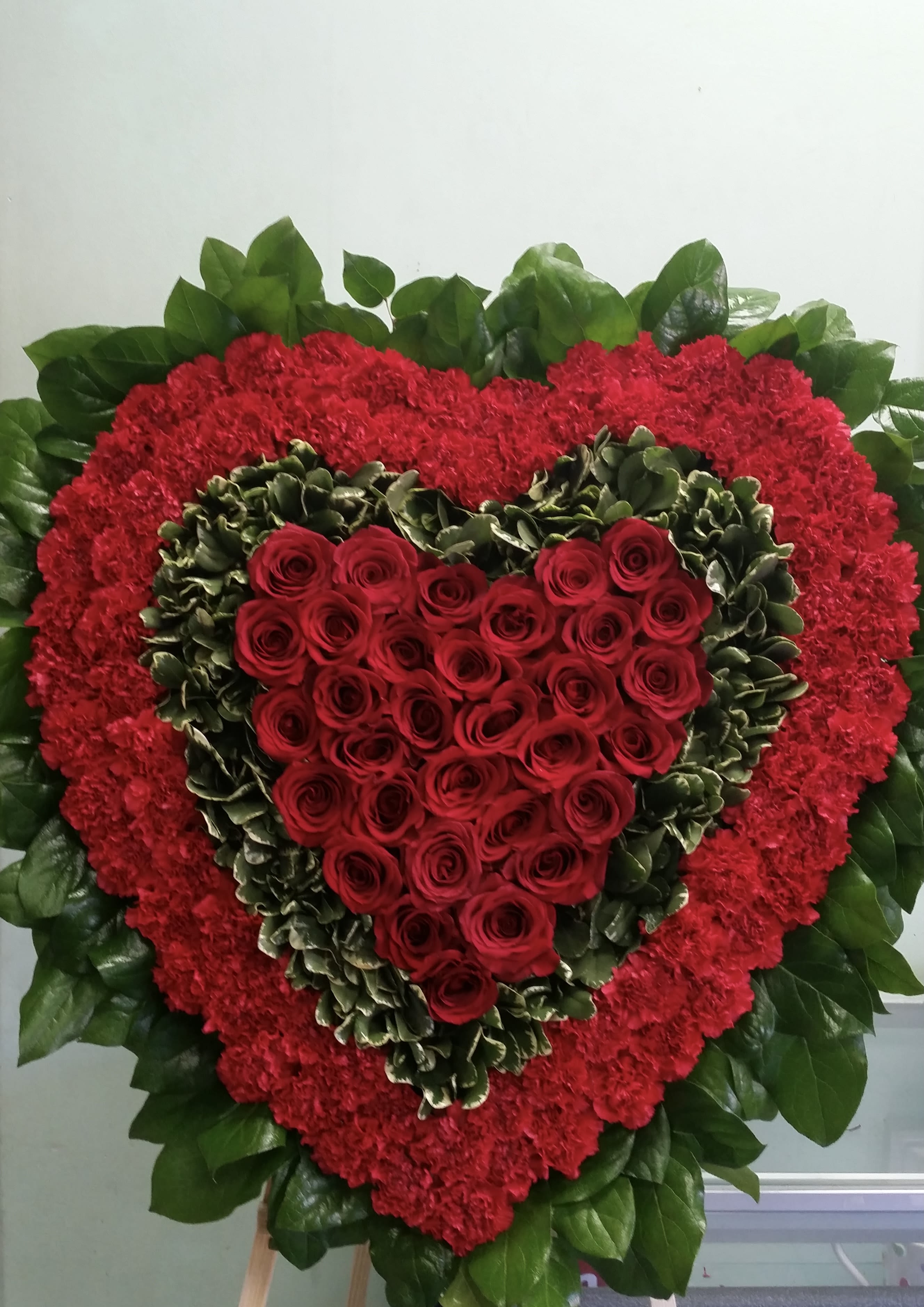 Heart-shaped red rose arrangement with red carnations and green foliage