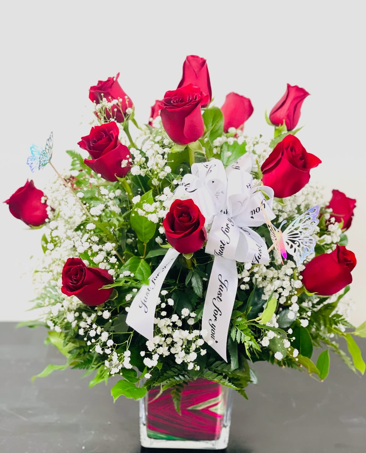 Red roses arranged in a clear square vase with white baby's breath and a white ribbon