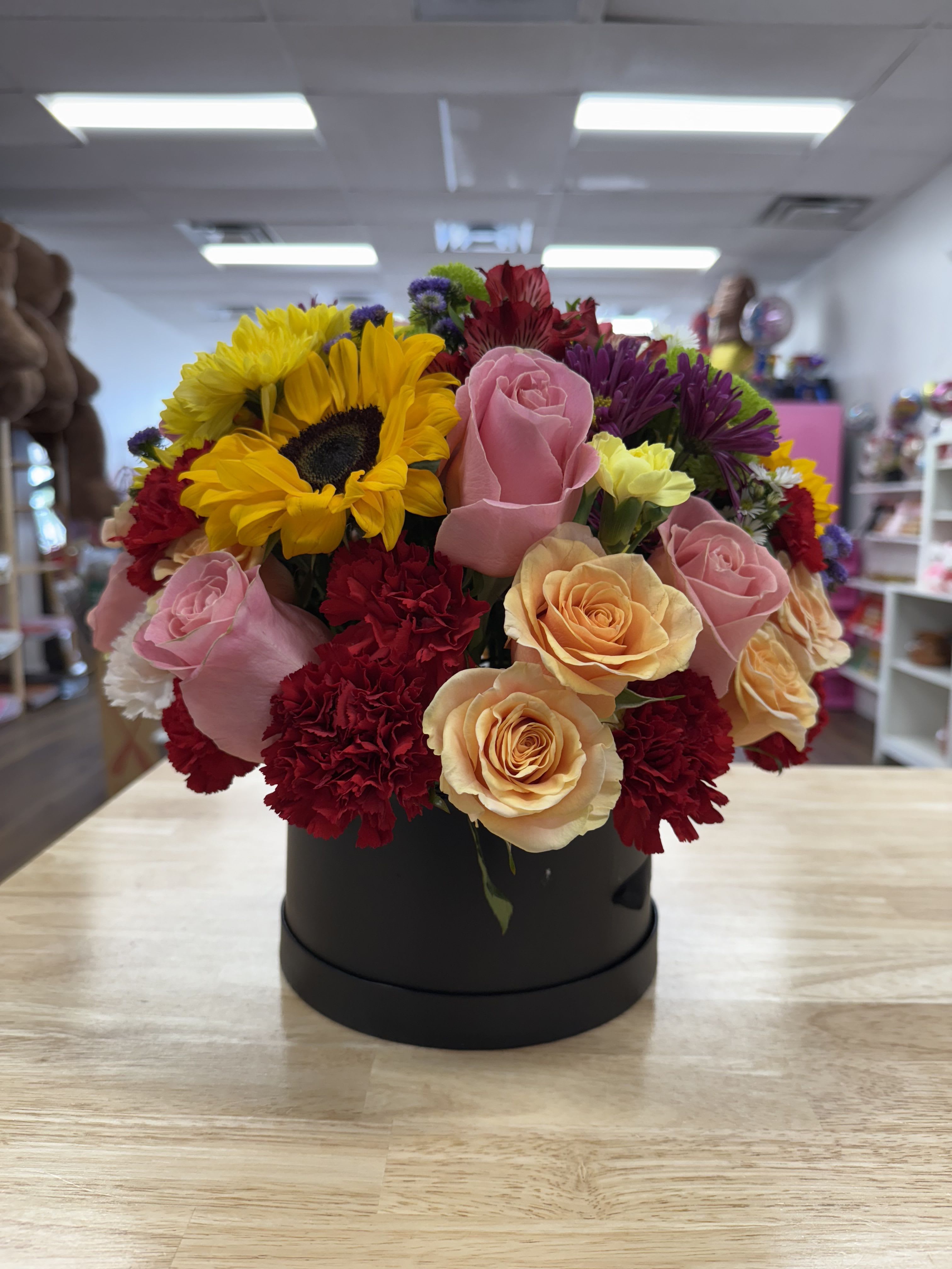 Mixed bouquet of sunflowers, roses, and carnations in a black box