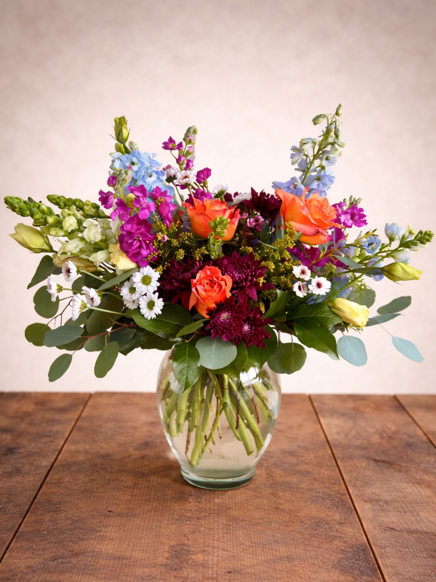 Mixed bouquet of orange, purple, and blue flowers in a clear glass vase