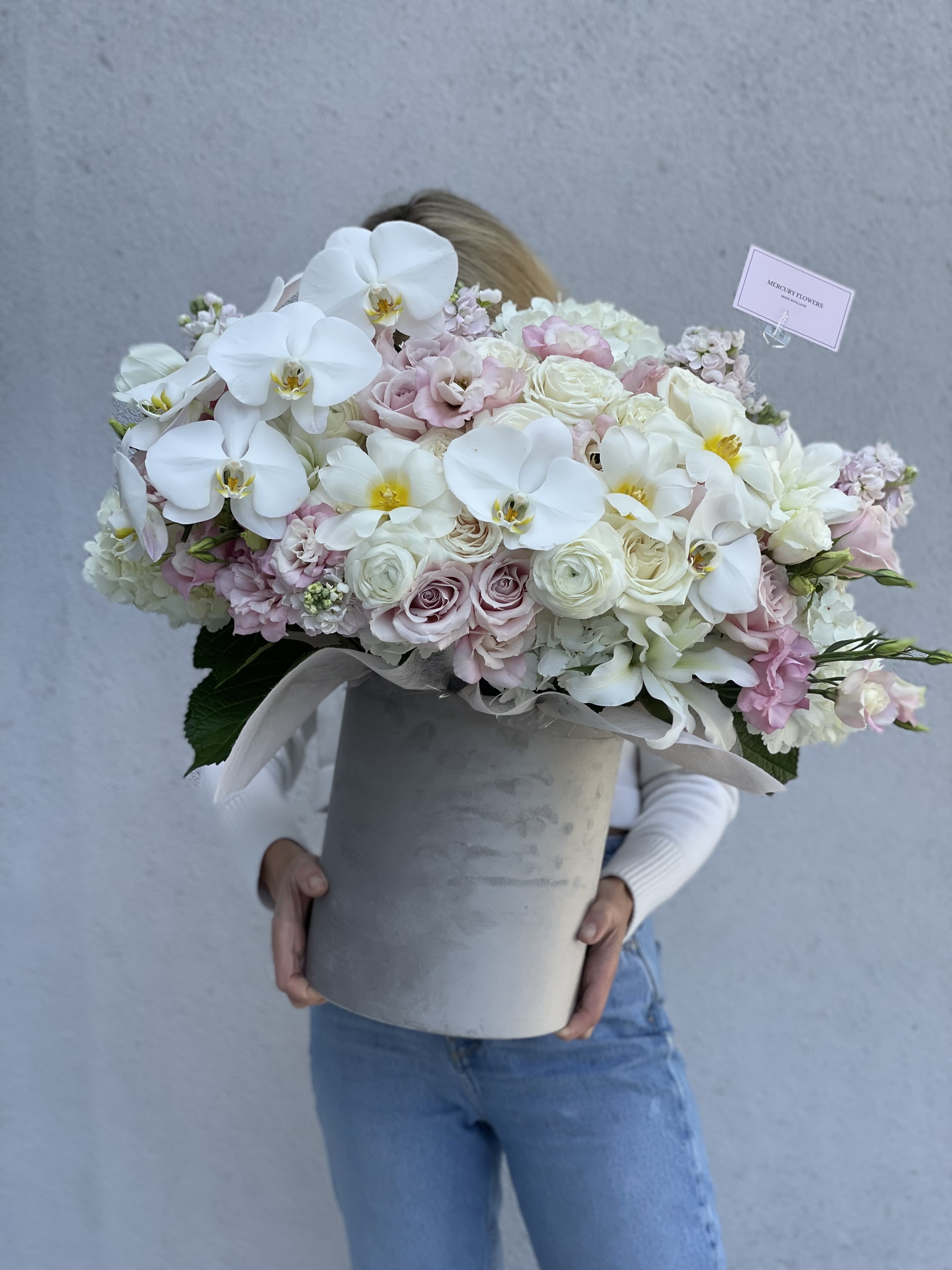 Large pastel bouquet with white orchids and pale roses in a gray hatbox