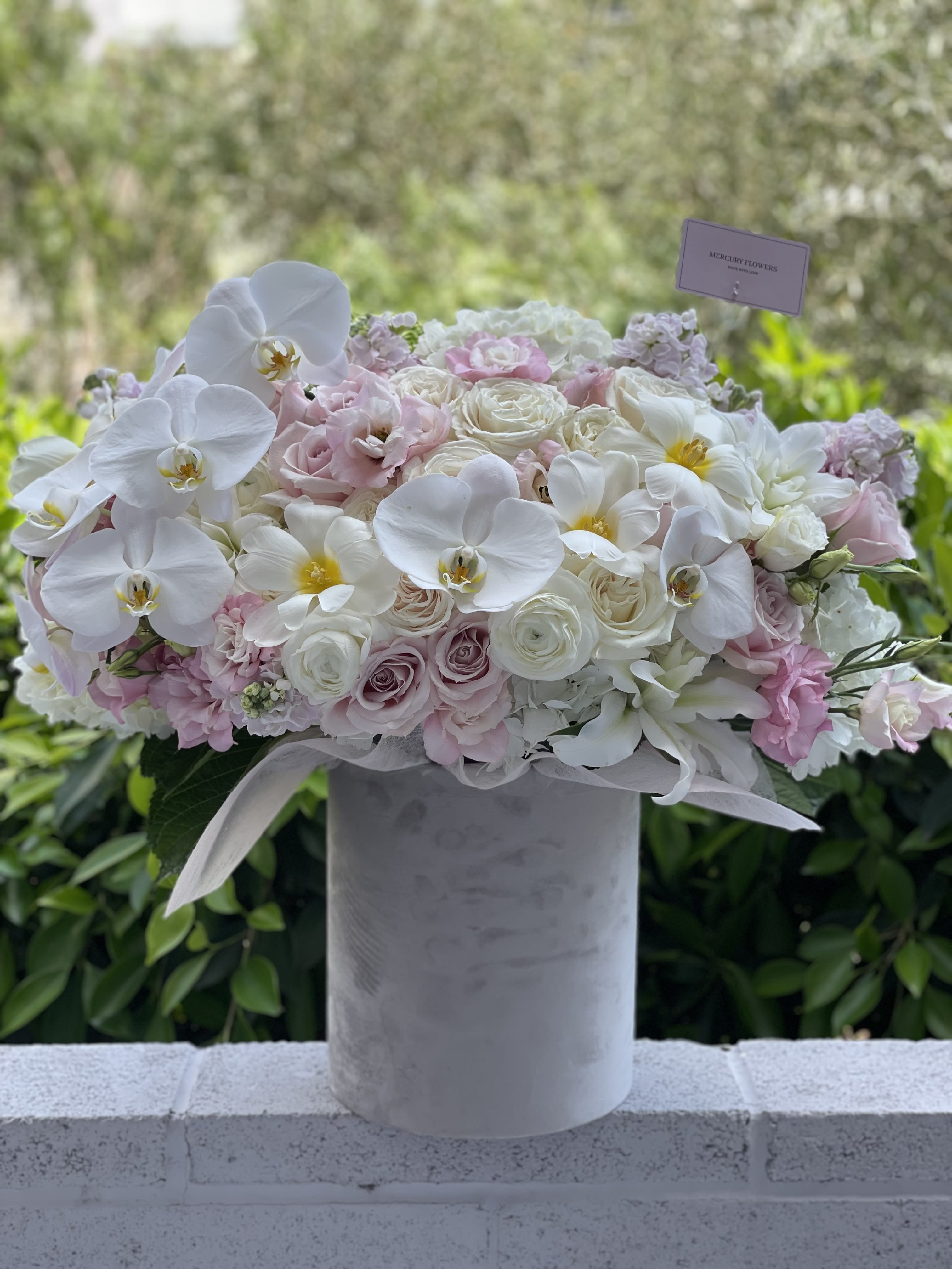 White orchids and blush roses arranged in a tall gray vase