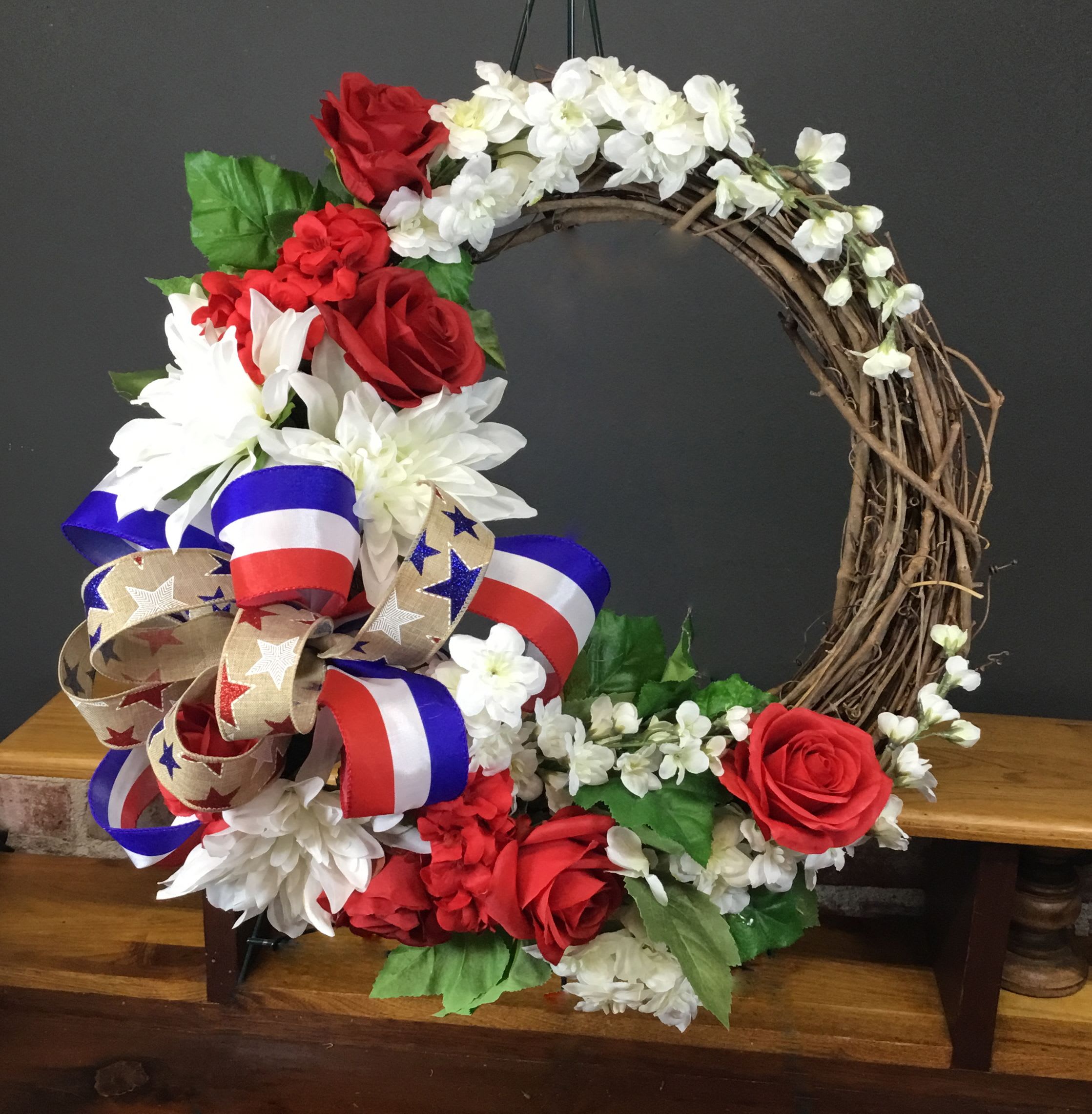 Patriotic SILK/ARTIFICIAL Wreath - A grapevine wreath dressed in red roses, white daisy-style blooms and delicate white filler makes a heartfelt patriotic statement-perfect as a sympathy or funeral tribute or for Memorial Day and Fourth of July displays. This artificial flower arrangement wreath carries the visual warmth of fresh flowers while offering lasting beauty for a housewarming gift or year-round front-door décor, letting the person you're honoring feel remembered and seen.