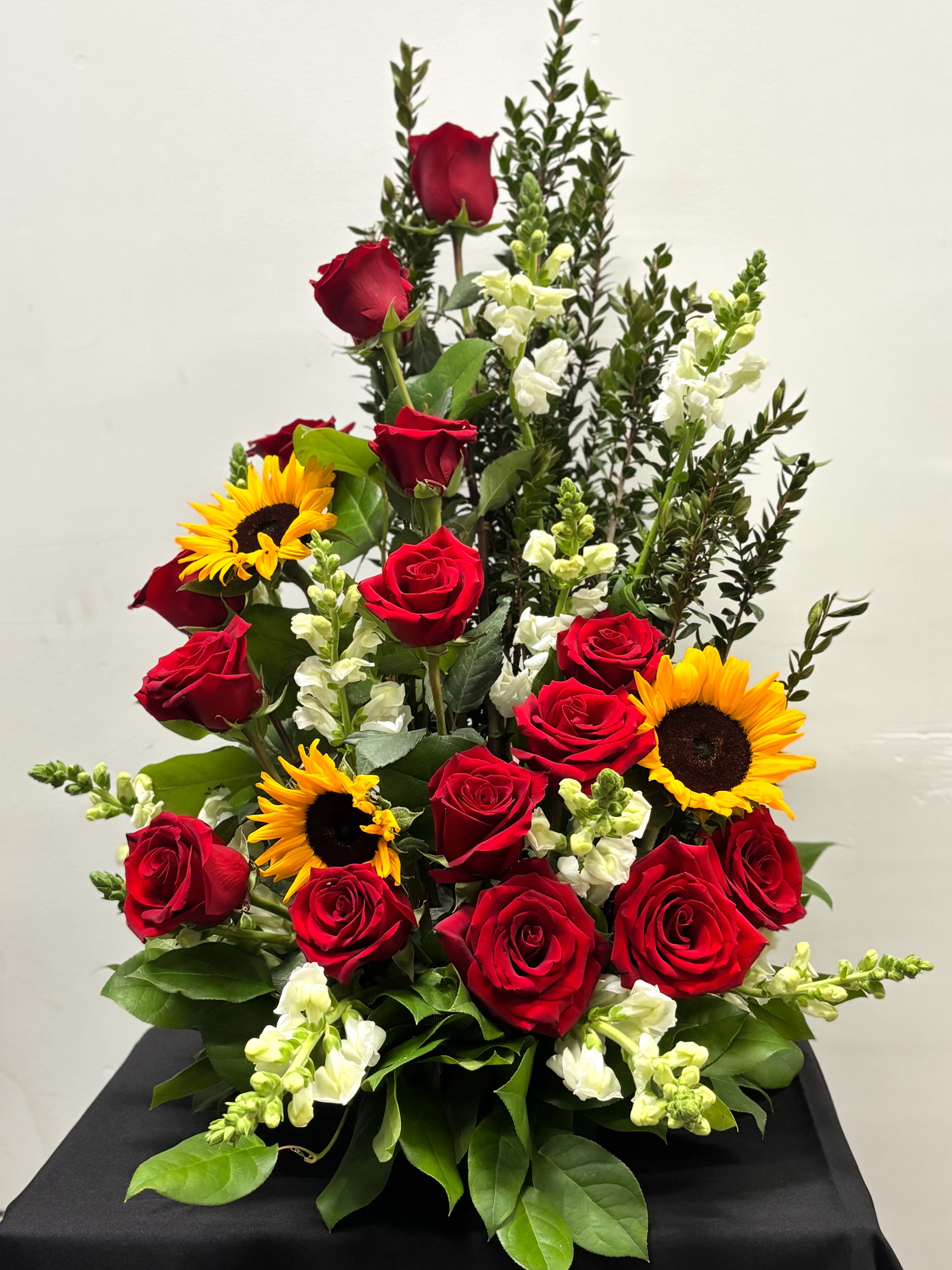 Tall arrangement of red roses, yellow sunflowers, and white snapdragons in a fan-shaped design