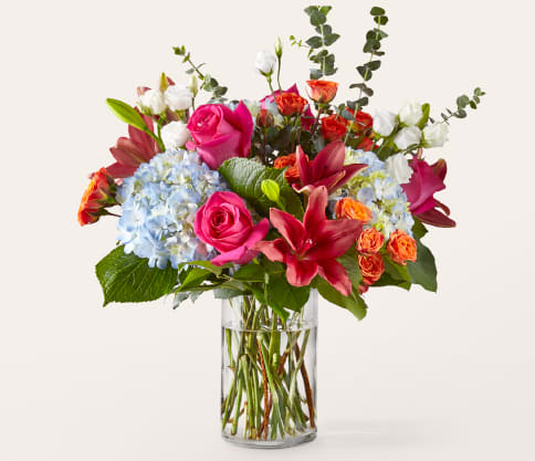Mixed bouquet of pink roses, lilies, and blue hydrangeas in a glass vase