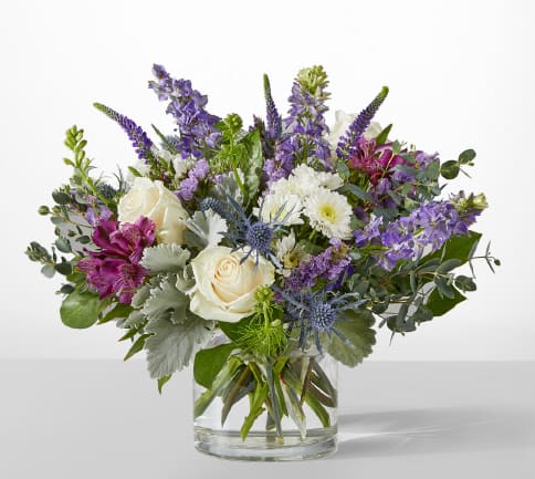 Mixed bouquet of white roses, purple flowers, and blue thistles in a glass vase